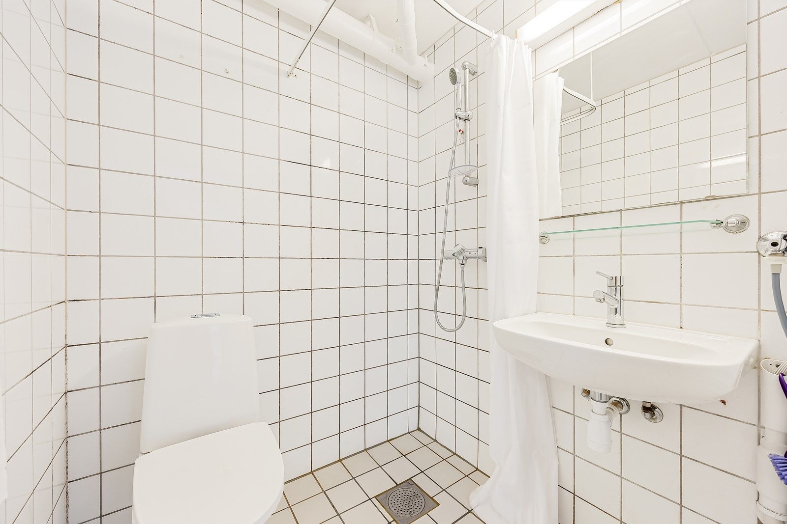 Badet er utstyrt med dusj på gulv, servant og klosett. Galleribilde