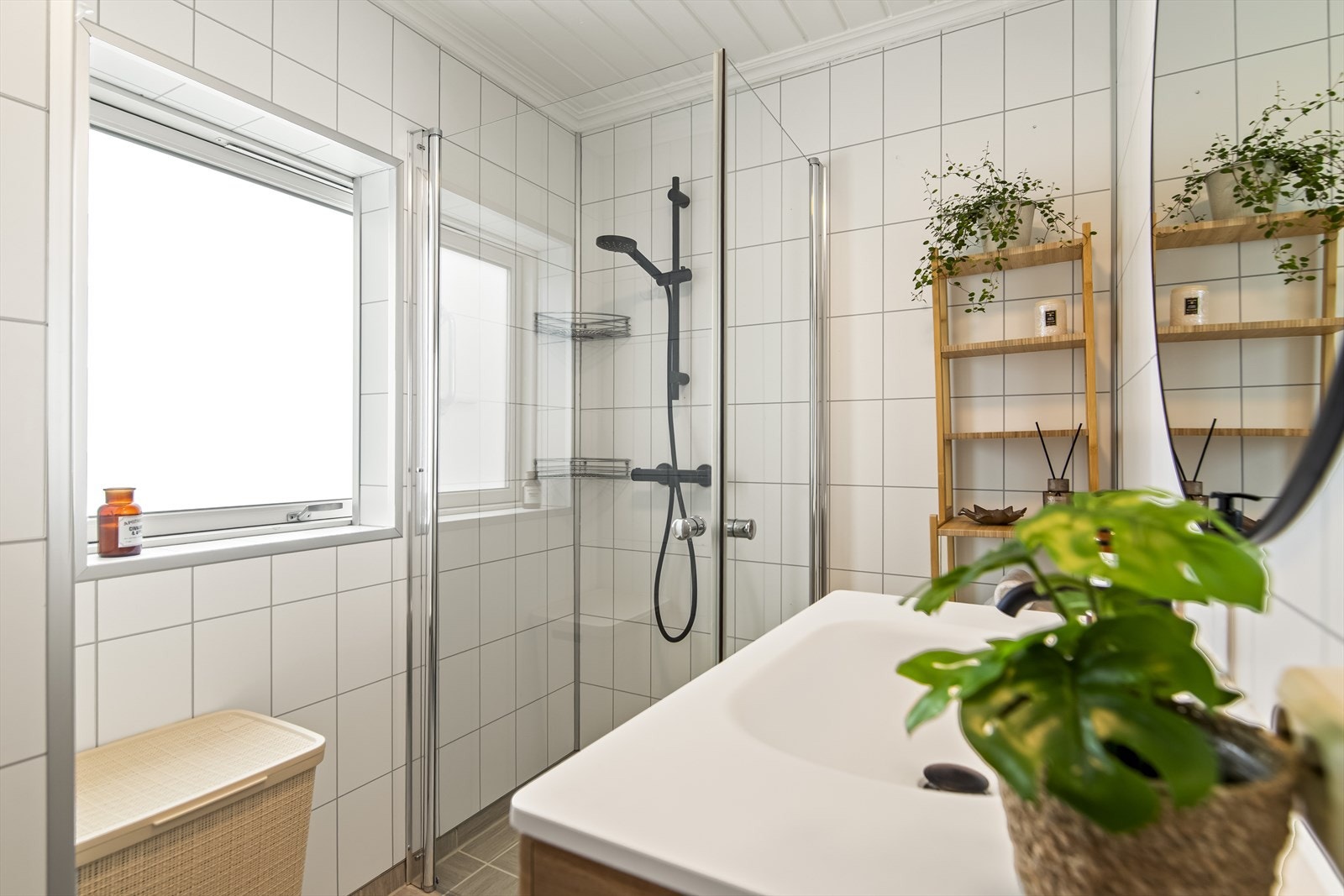 Badet inneholder praktisk dusjnisje med glassdører, vegghengt toalett og et vindu som slipper inn naturlig dagslys. Galleribilde