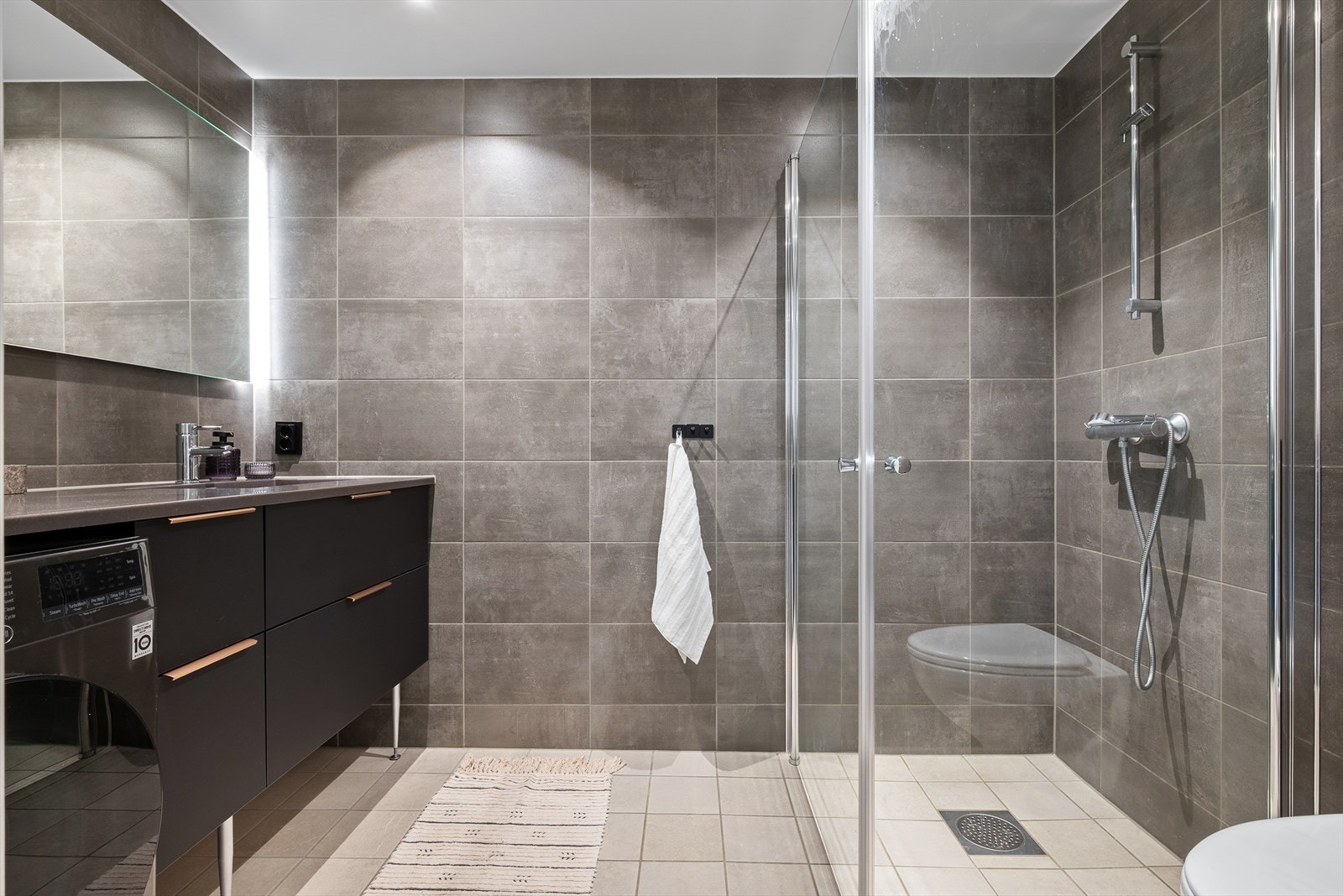 Badet har flislagte vegger og gulv i smakfulle farger, og rikelig med skuffeplass under servanten. Galleribilde