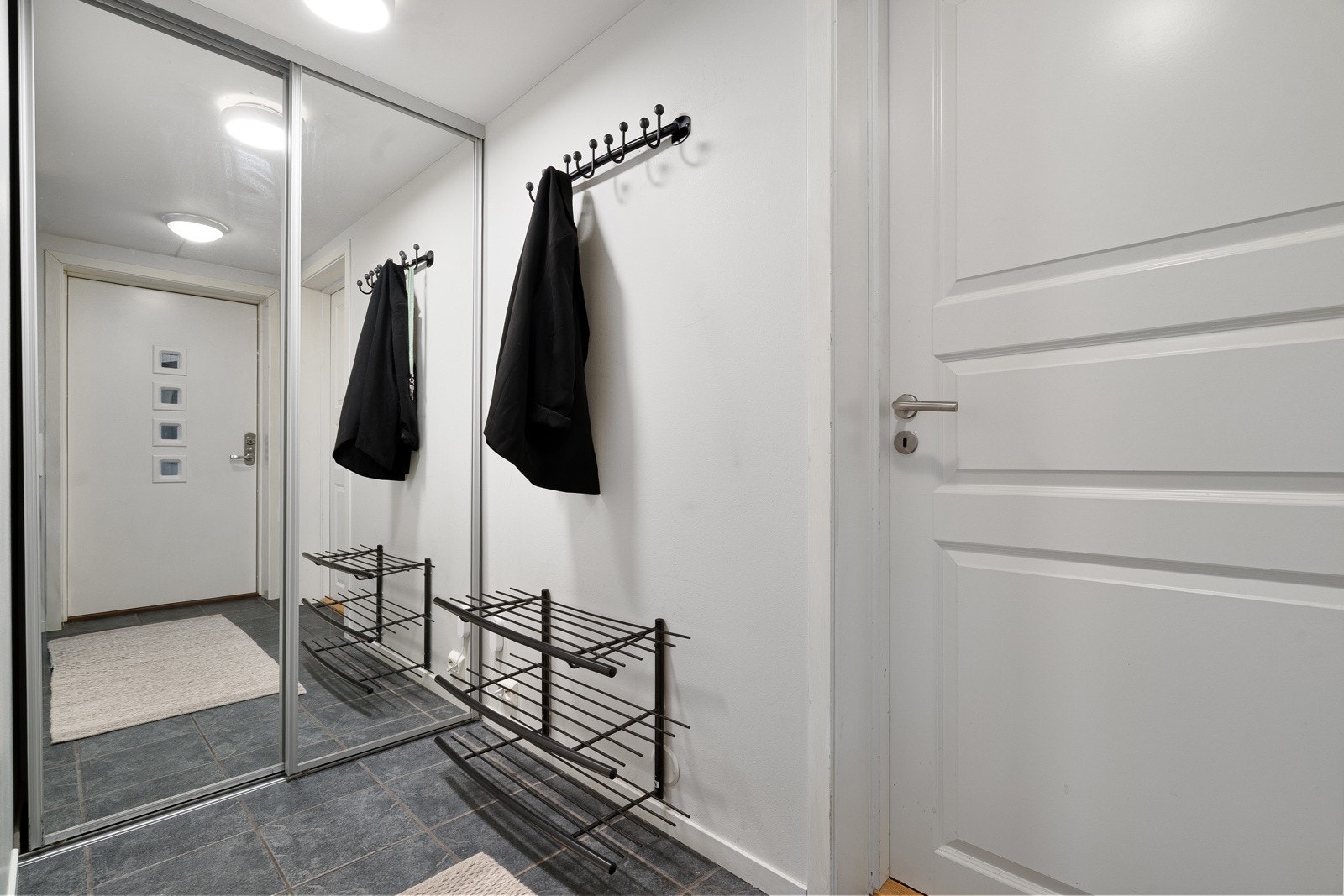 En lys entré med fliser på gulv, gulvvarme og skyvedørsgarderobe med speildører.