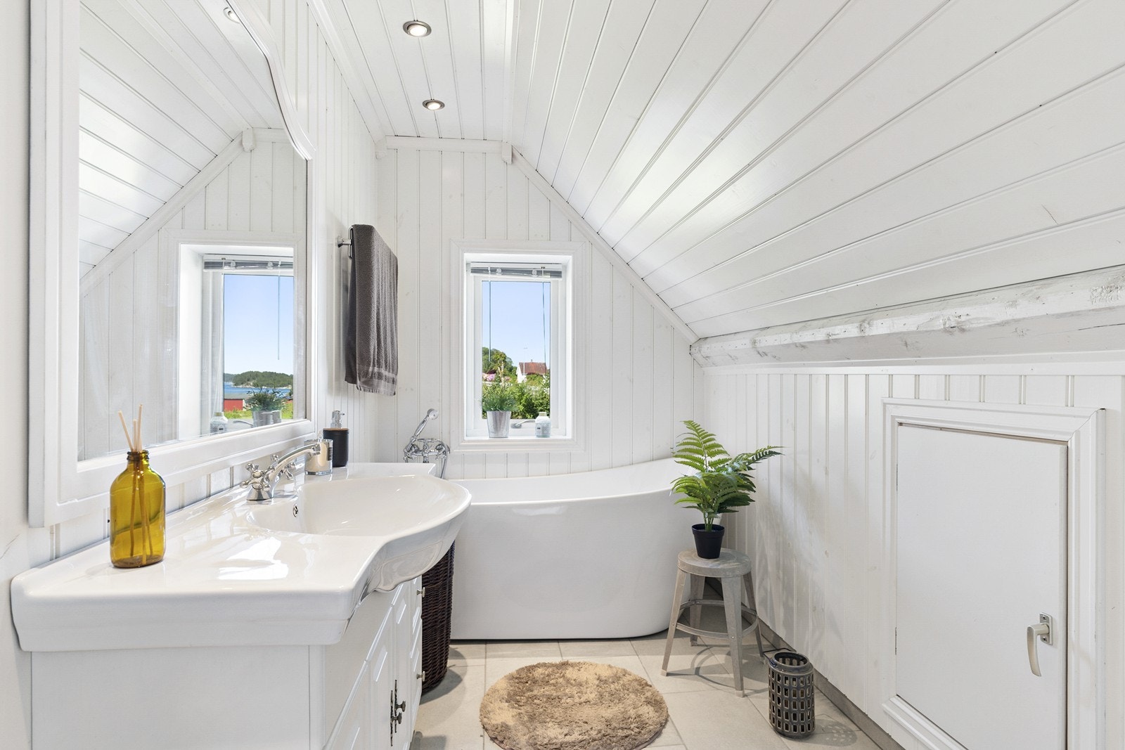 Badet er romslig og innredet med gulvfliser med varmekabler, panel på vegger og i tak, samt vegghengt toalett, baderomsinnredning med servant og badekar. Galleribilde