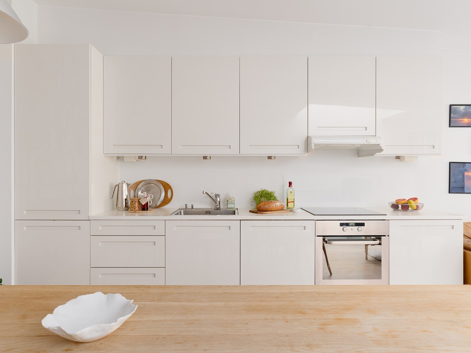 Stilrent HTH-kjøkken fra 2010 med hvite, glatte, høyglans fronter, laminat benkeplate med kum i rustfritt stål og ett-greps blandebatteri. Galleribilde