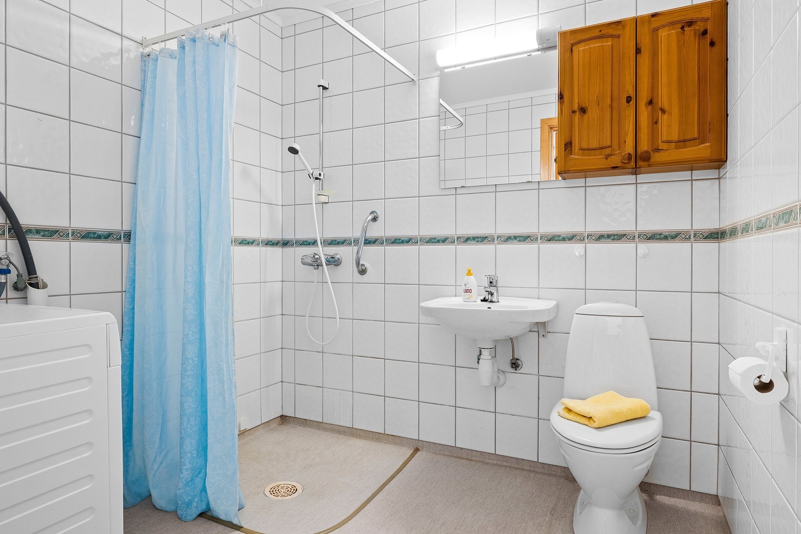 Bad med fliser på vegg, belegg på gulv, opplegg for vaskemaskin og avtrekksventilasjon. Galleribilde