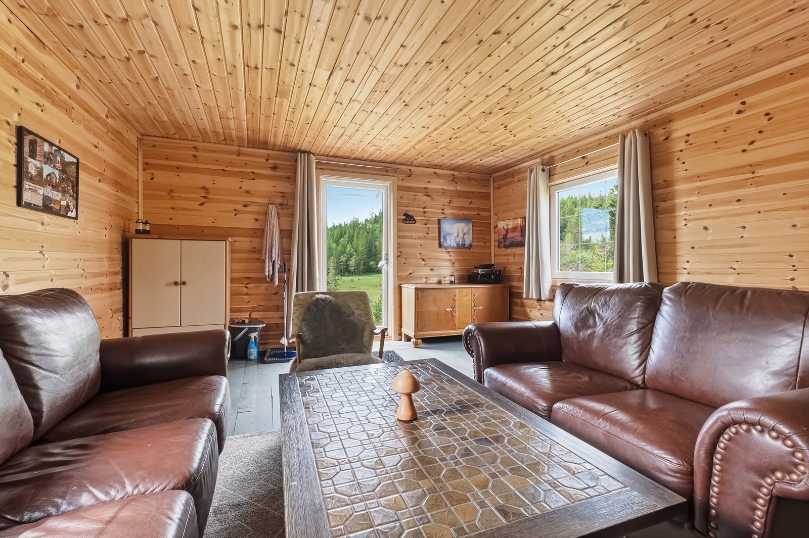 Hyttestue med panelte overflater, god takhøyde og vinduer som slipper naturen inn. Galleribilde