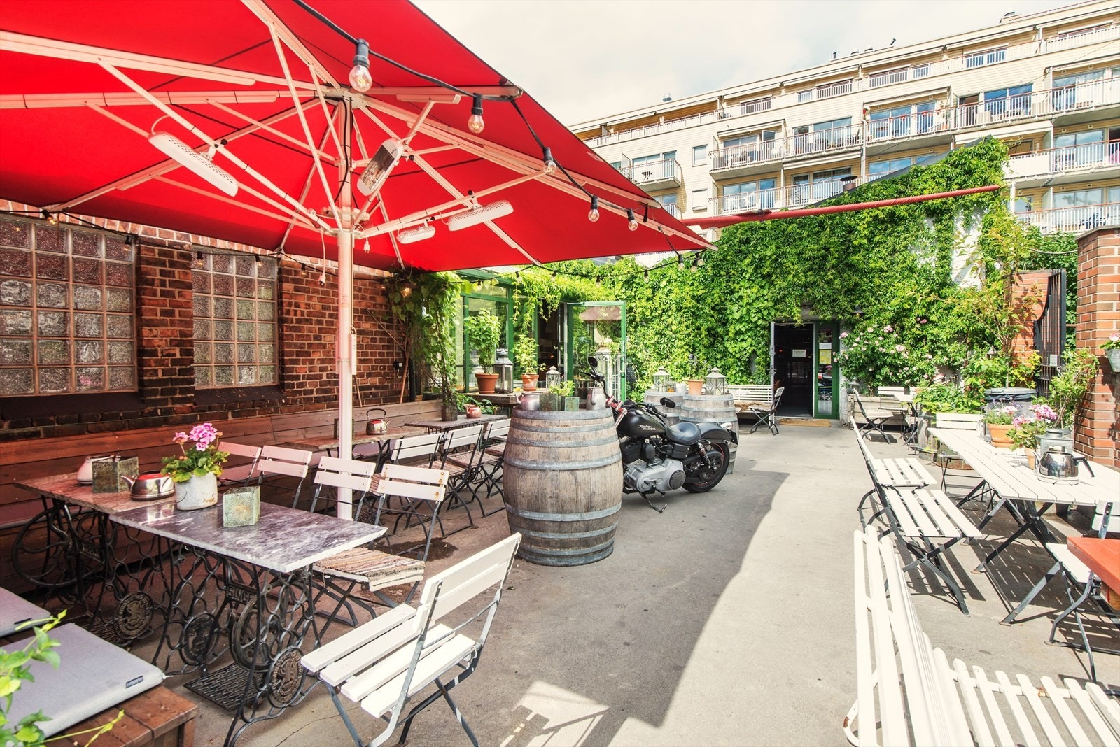 Oslo Mekaniske Verksted. Avslappet stemning og uteservering med grønne planter, langbord og benker. Galleribilde