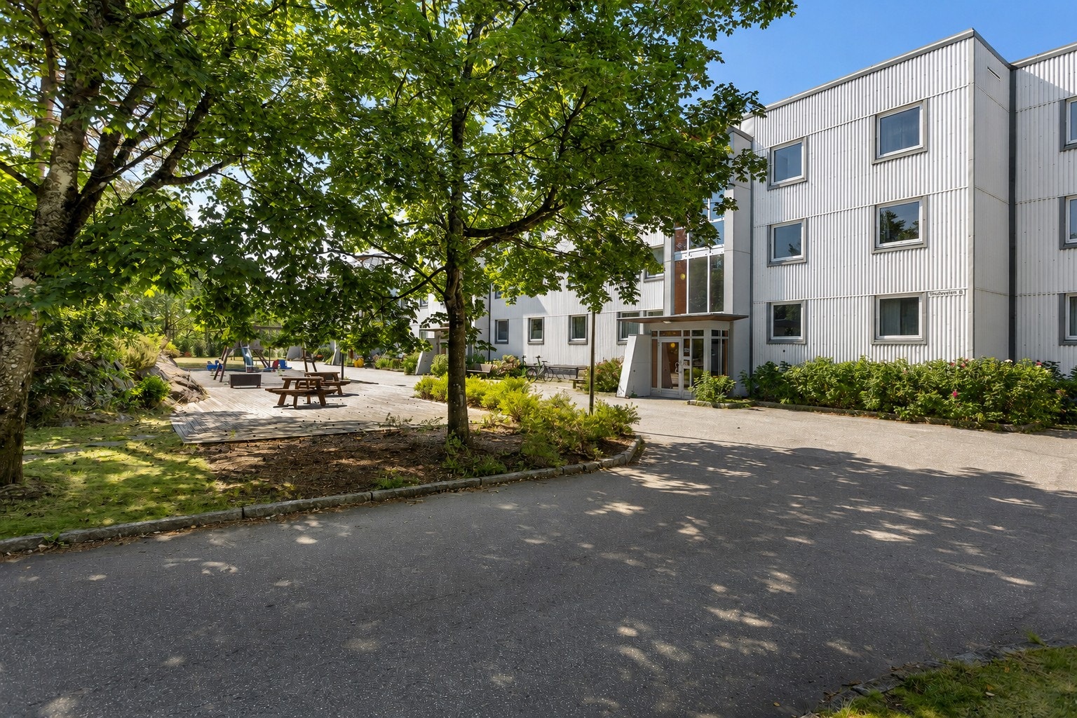 Tomten er pent opparbeidet med asfalterte gangveier, lekeplass, benker, plen og beplantning. Galleribilde