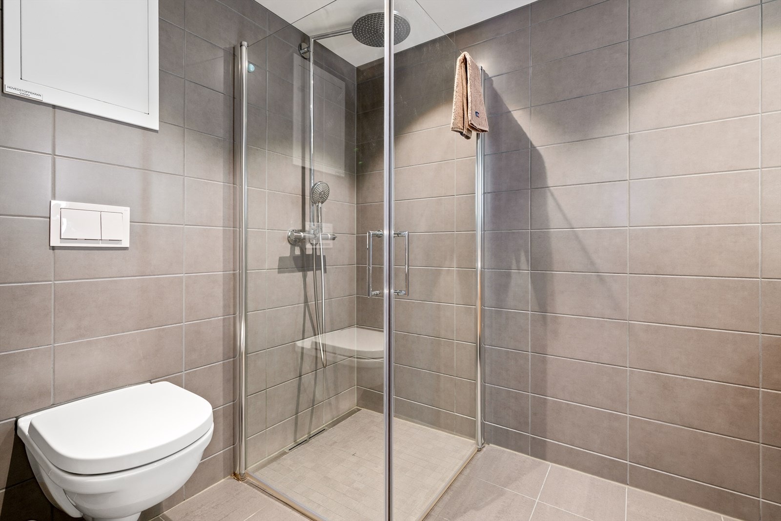 Badet er innredet med heldekkende servant, speil med belysning, veggmontert toalett og innfellbare dusjvegger/hjørne i herdet glass Galleribilde