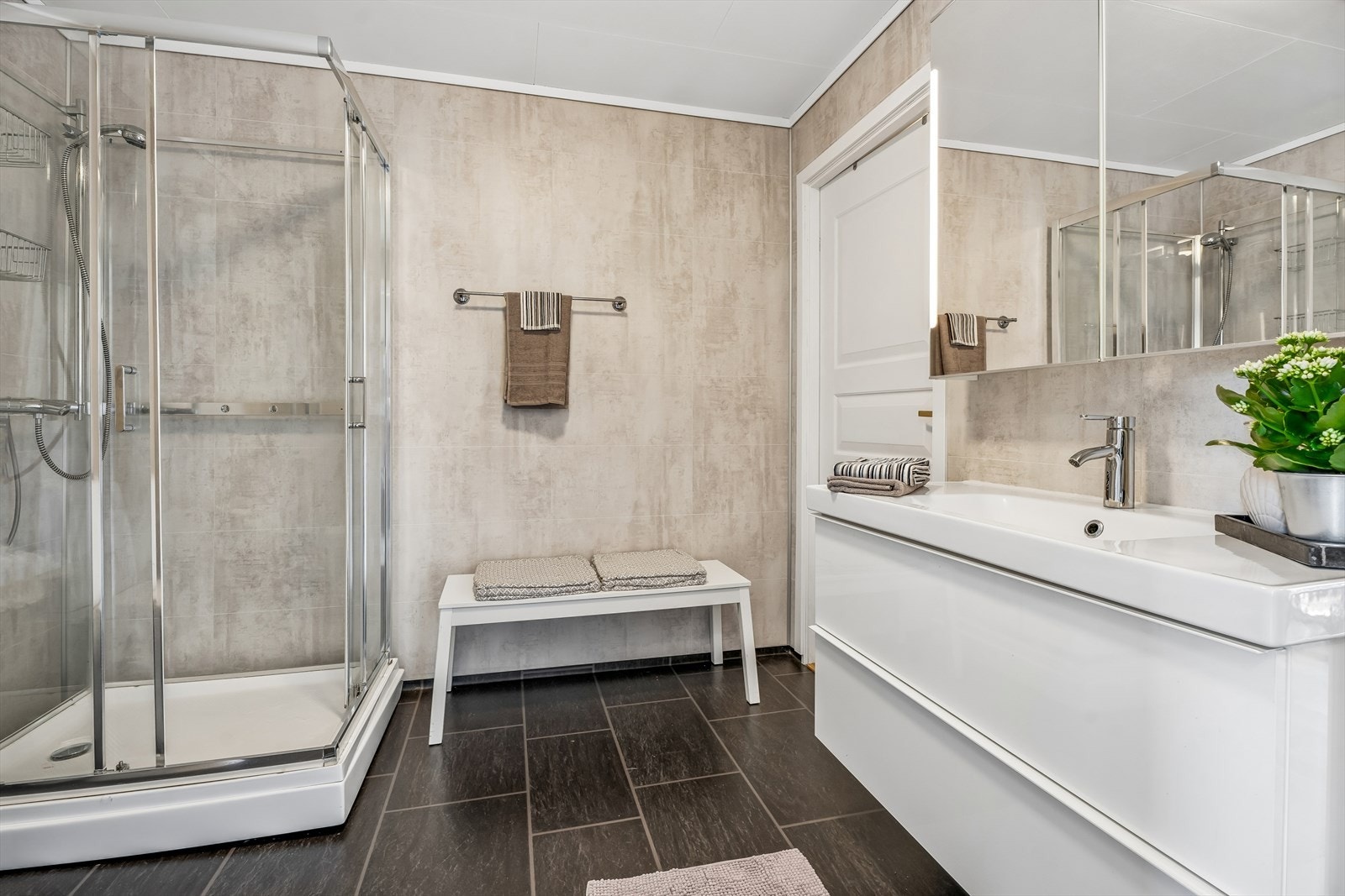 Badet er utstyrt med baderomsinnredning med servant og skuffer, speilskap, gulvmontert toalett og dusjkabinett. Galleribilde