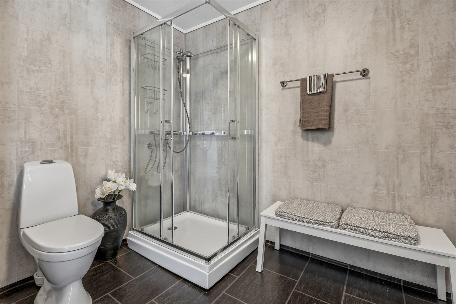 Bad med baderomsplater på vegg, gulvbelegg og gulvvarme. Rett innenfor badet finner vi vaskerom/teknisk rom. Galleribilde