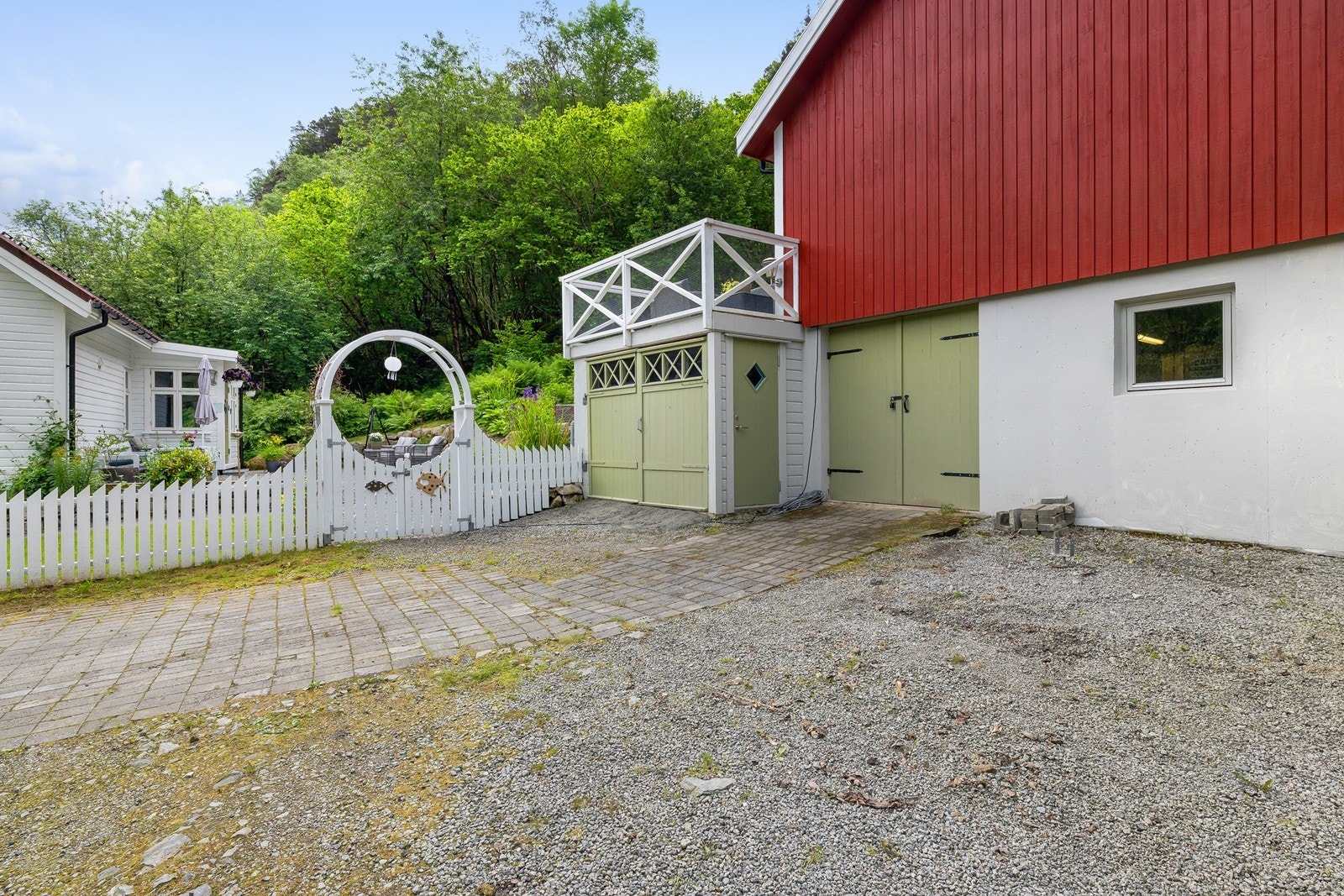 Koselig tunmiljø med hvitt stakittgjerde, port og flere bygg som sammen skaper et sjarmerende gårdspreg. Galleribilde