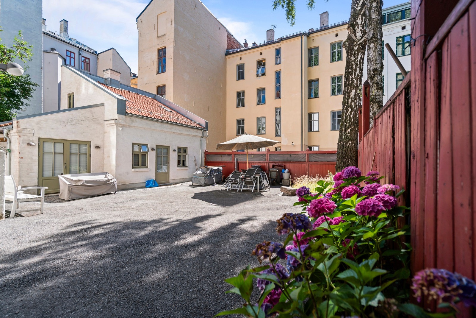 Koselig bakgård med sittegrupper og frodige blomsterbed. Galleribilde
