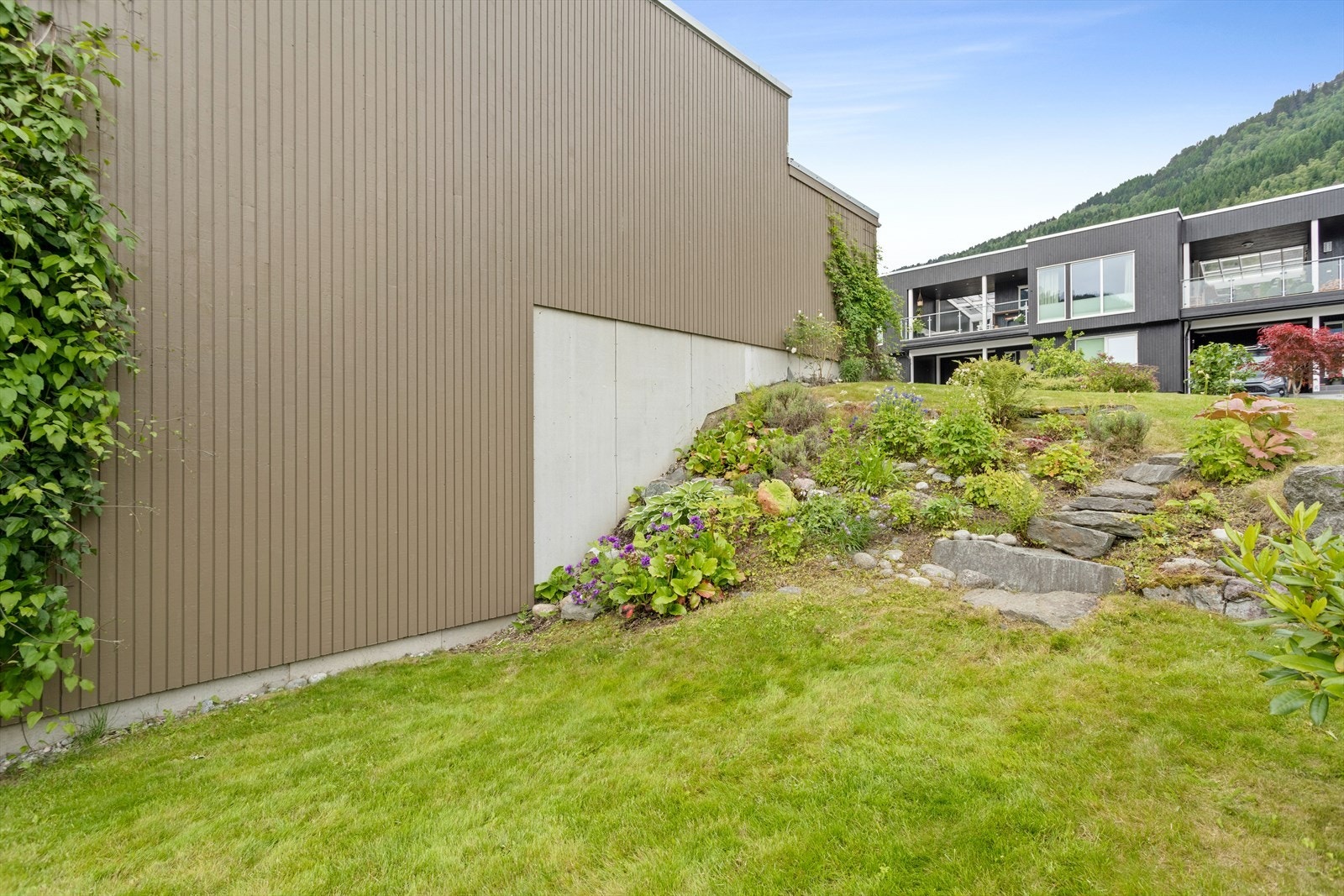 Pent opparbeidde uteområde med natursteinsbed, variert beplanting og grøne soner. Galleribilde