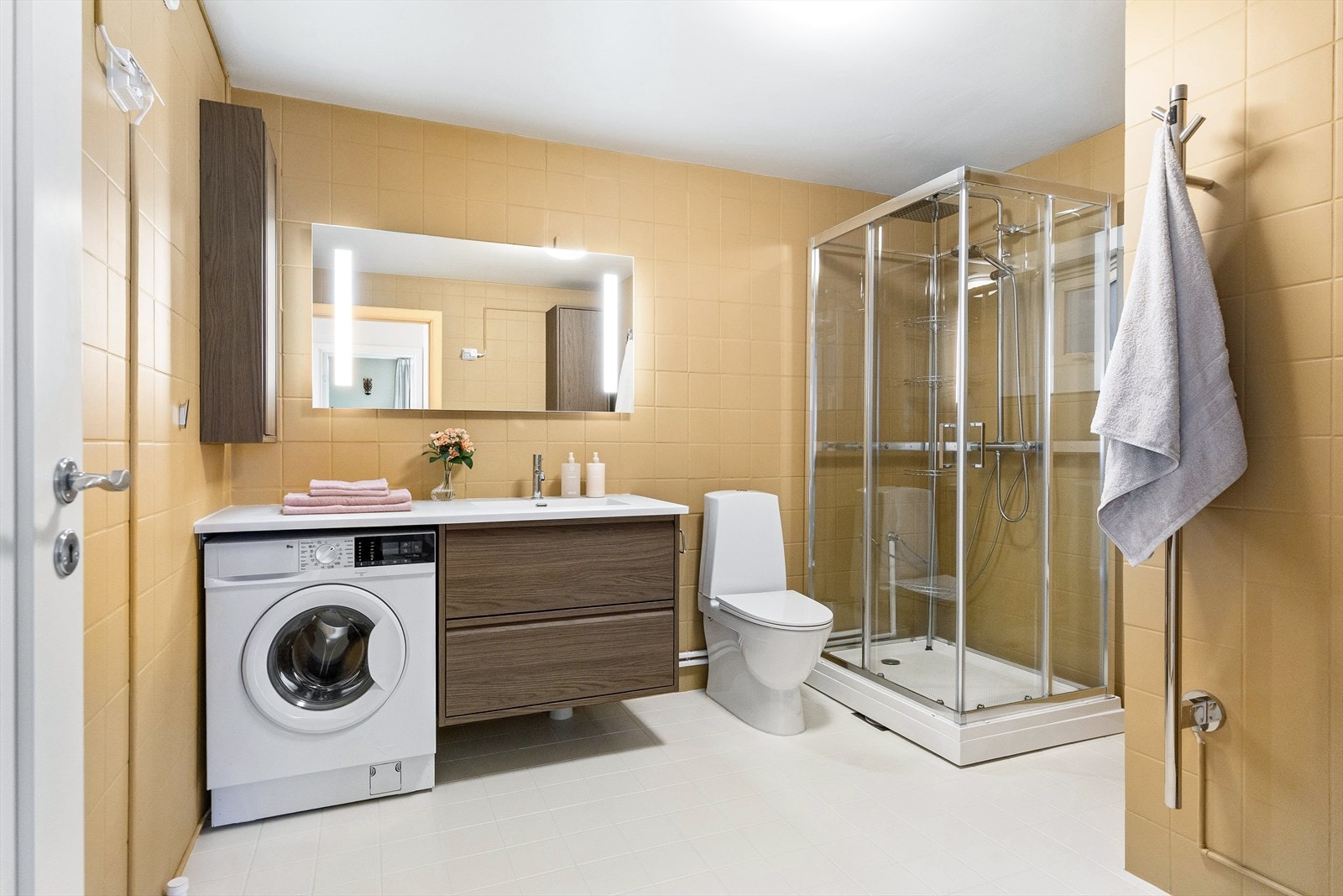 Badet er utstyrt med servantskap med benkeplate og nedfelt servant, speil med innebygd belysning, veggskap, gulvmontert klosett og dusjkabinett. Galleribilde