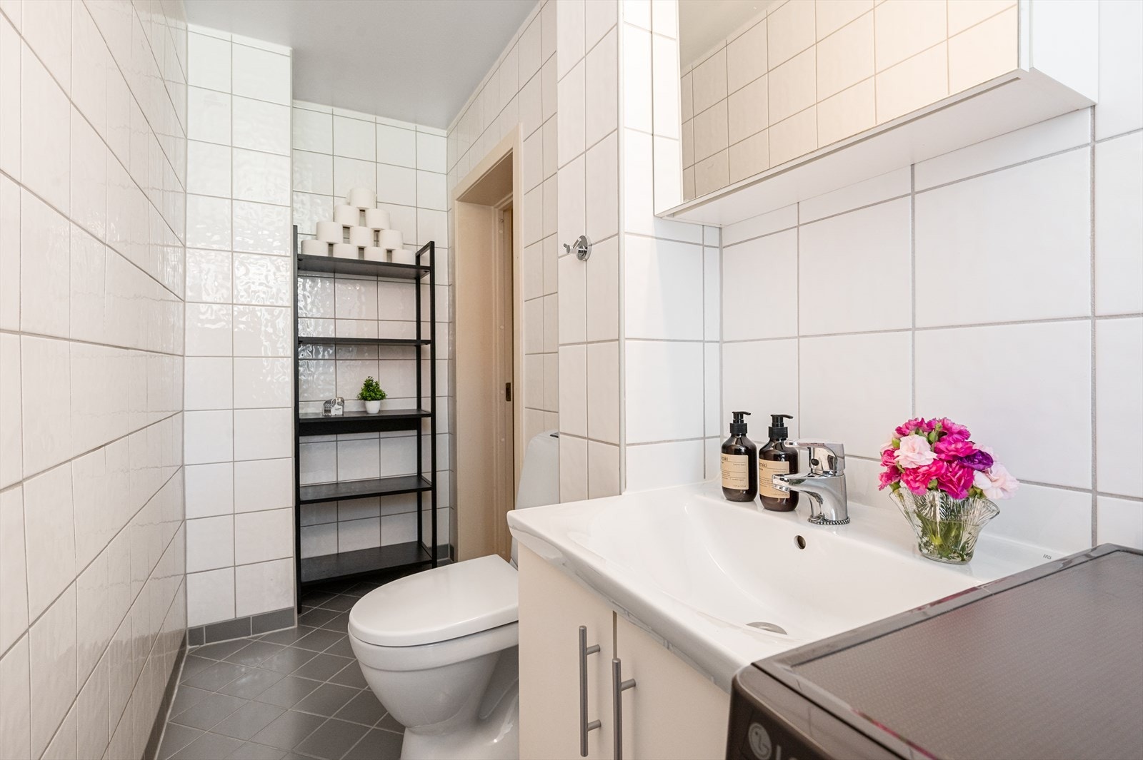 Innredningen består av dusjhjørne med fastmontert gulvskinne med skyvedører, servantskap med med hvit servant og blandebatteri, gulvmontert toalett og opplegg for vaskemaskin. Galleribilde