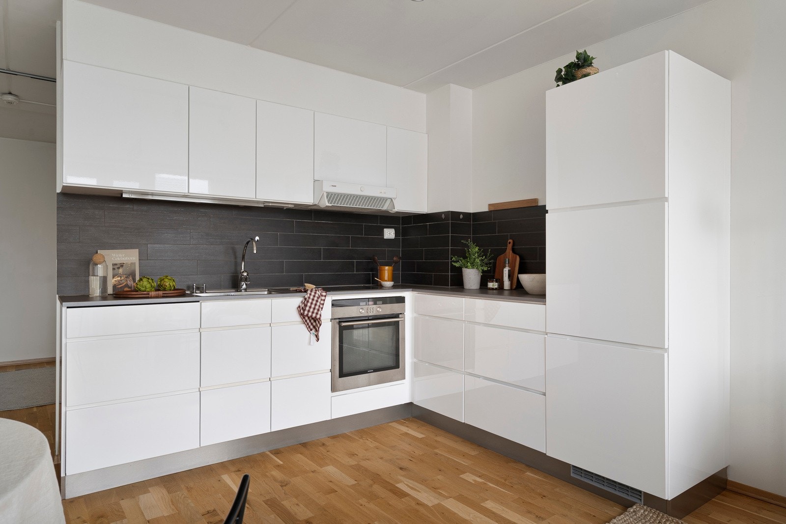 Kjøkkenet fremstår som stilrent og moderne, med flislagt vegg bak benkeplate og belysning under overskap.