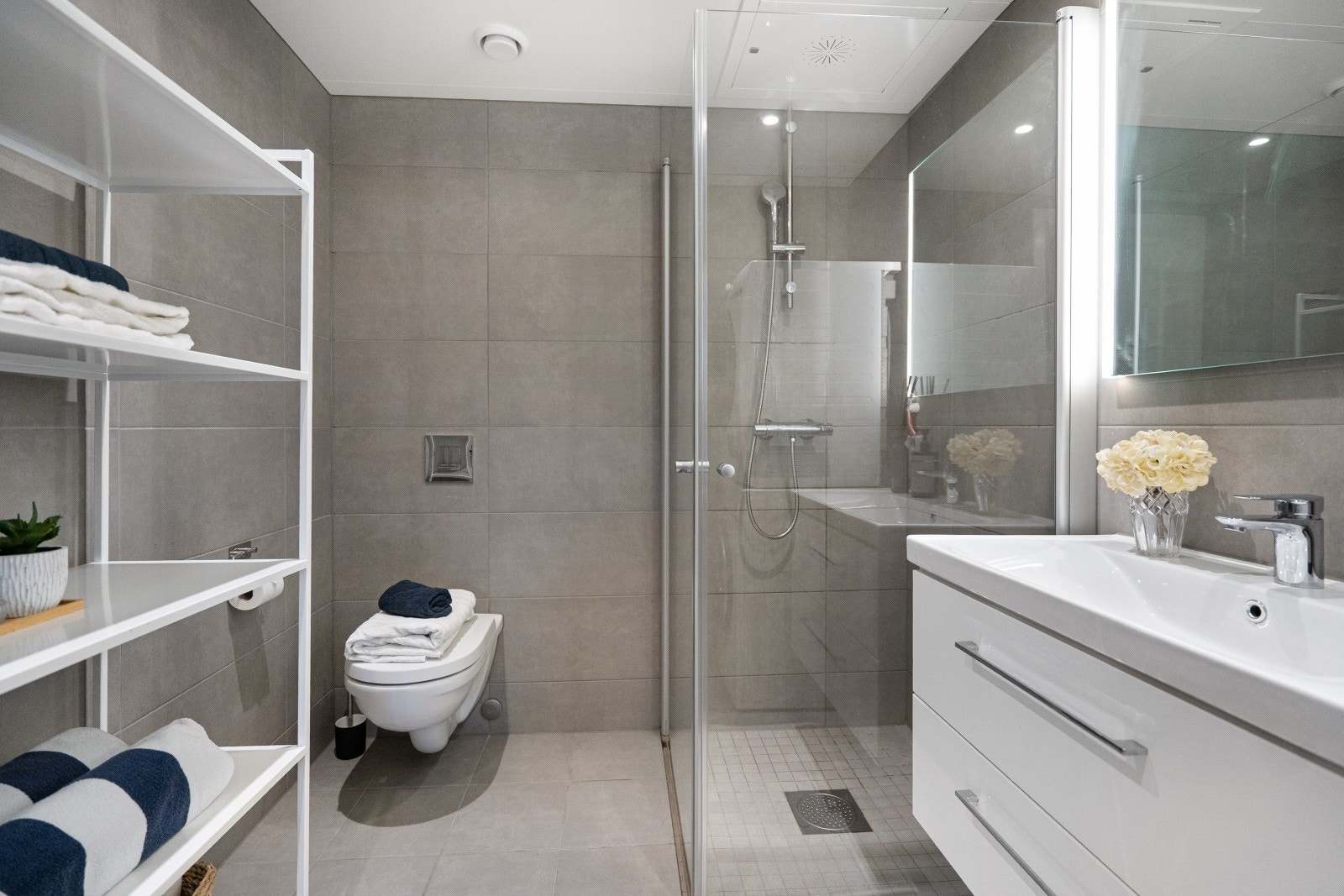 Badet er innredet med veggmontert toalett, dusjhjørne og servantinnredning med nedfelt servant. Galleribilde