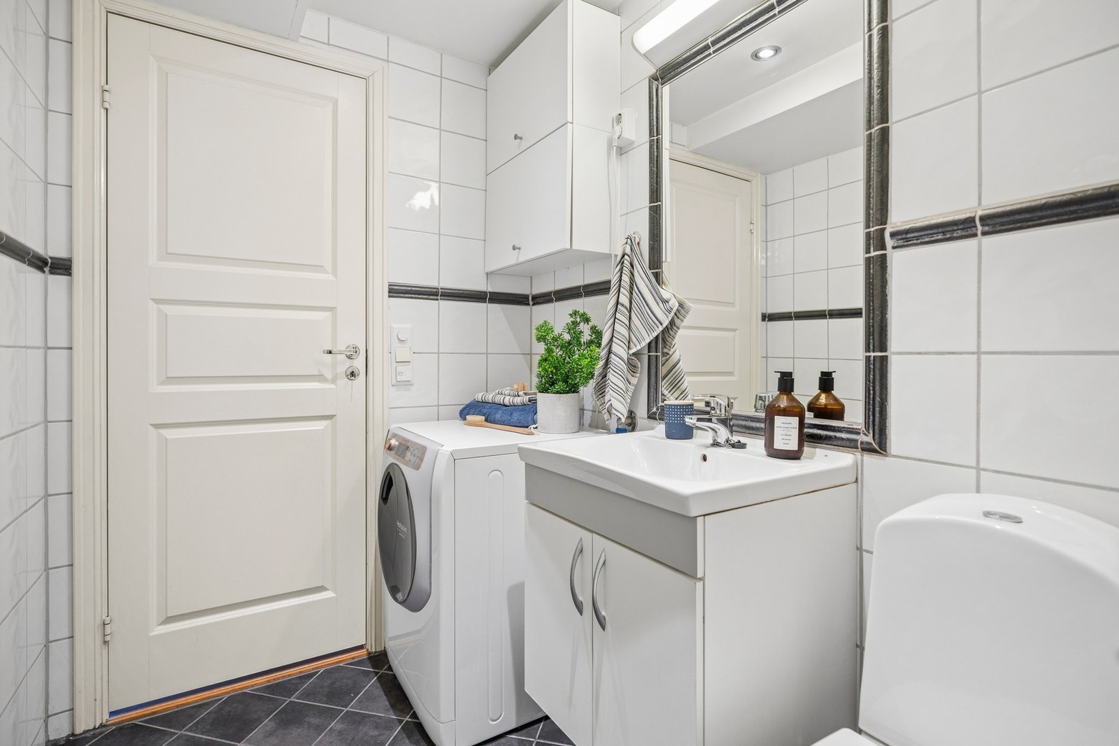 Badet er innredet med servant med underskap og speil, vegghengt oppbevaringsskap, dusjhjørne med glassdører, toalett samt opplegg og plass til vaskemaskin. Galleribilde