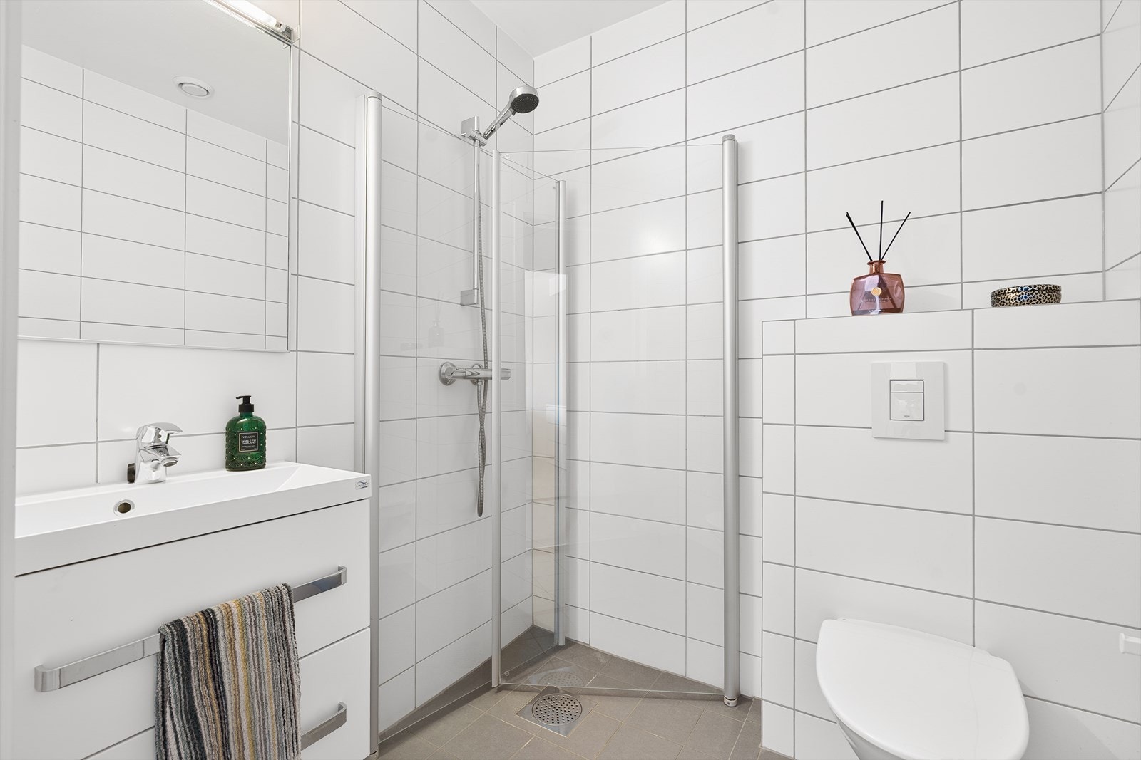 Stilrent og helfliset bad, moderne innredet med vegghengt toalett, dusjhjørne med foldbare glassvegger, hel servant og god oppbevaringsplass i baderomsmøbel. Galleribilde