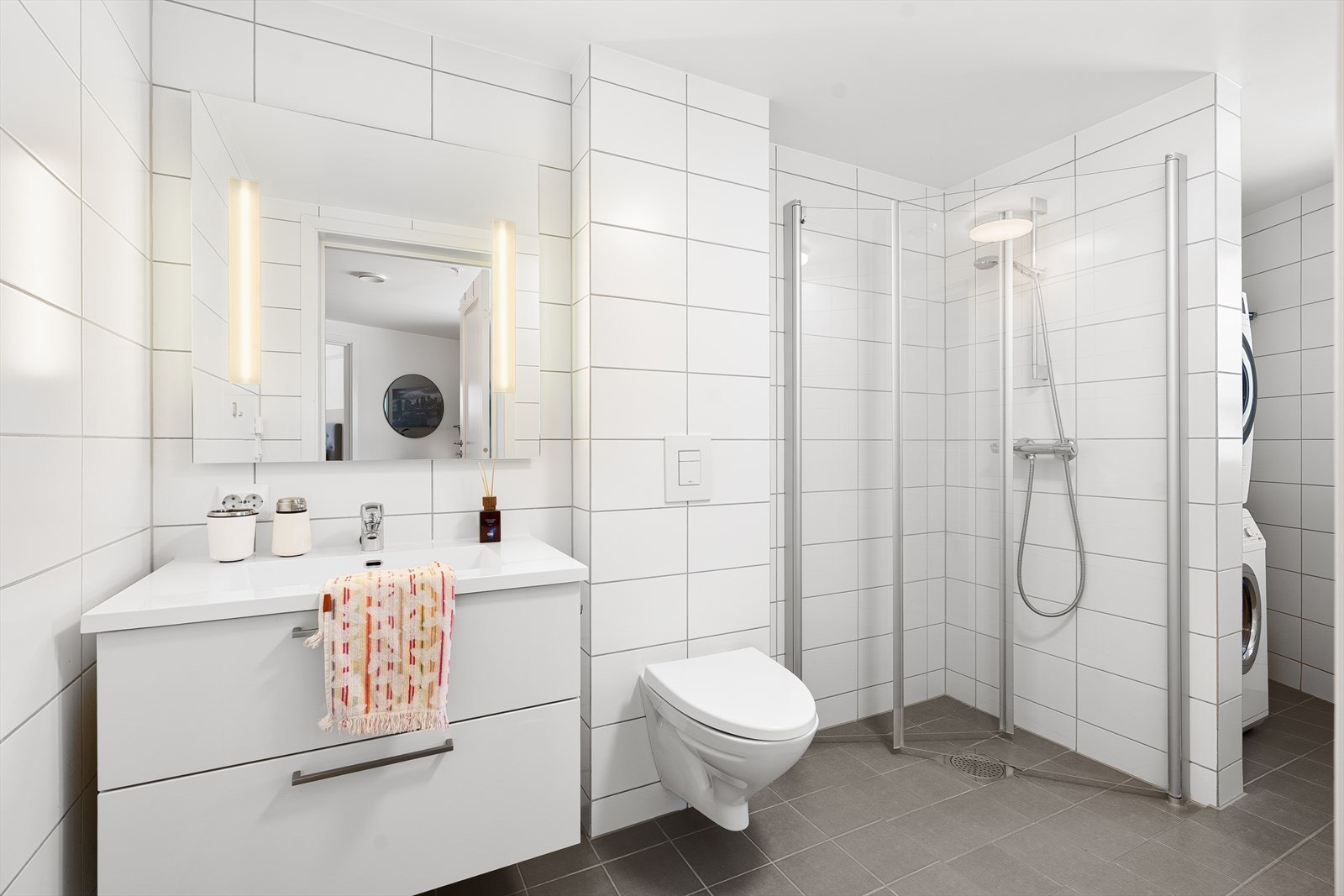 Helfliset bad med moderne innredning. Badet har vegghengt toalett, speil med belysning, dusjhjørne med foldbare glassvegger, hel servant og god oppbevaringsplass i baderomsmøbel. Galleribilde