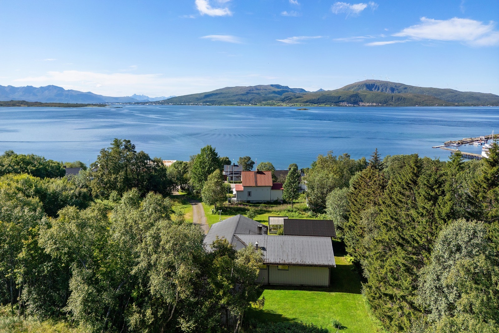 Dronebilde som viser boligen i naturskjønne omgivelser, med sjø og fjell rundt området. Galleribilde