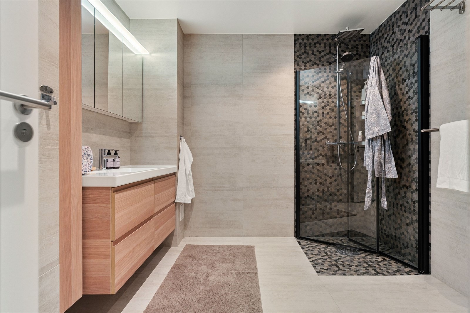 Fra gangen er det adkomst til badet som måler ca. 7 m². Et rålekkert og oppusset bad. Store og eksklusive 60x60 fliser og et dusjhjørne med fliser av sten, utstyrt med regndusj skaper en herlig atmosfære. Badet er også utstyrt med vegghengt toalett. Galleribilde