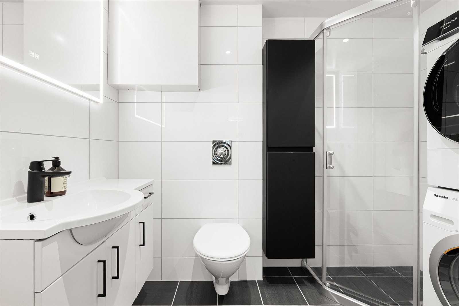 Bad nr. 2 er helfliset med moderne innredning og praktisk vaskeromsløsning. Badet har vegghengt toalett, dusjhjørne, speil med belysning og opplegg til vaskemaskin. Galleribilde