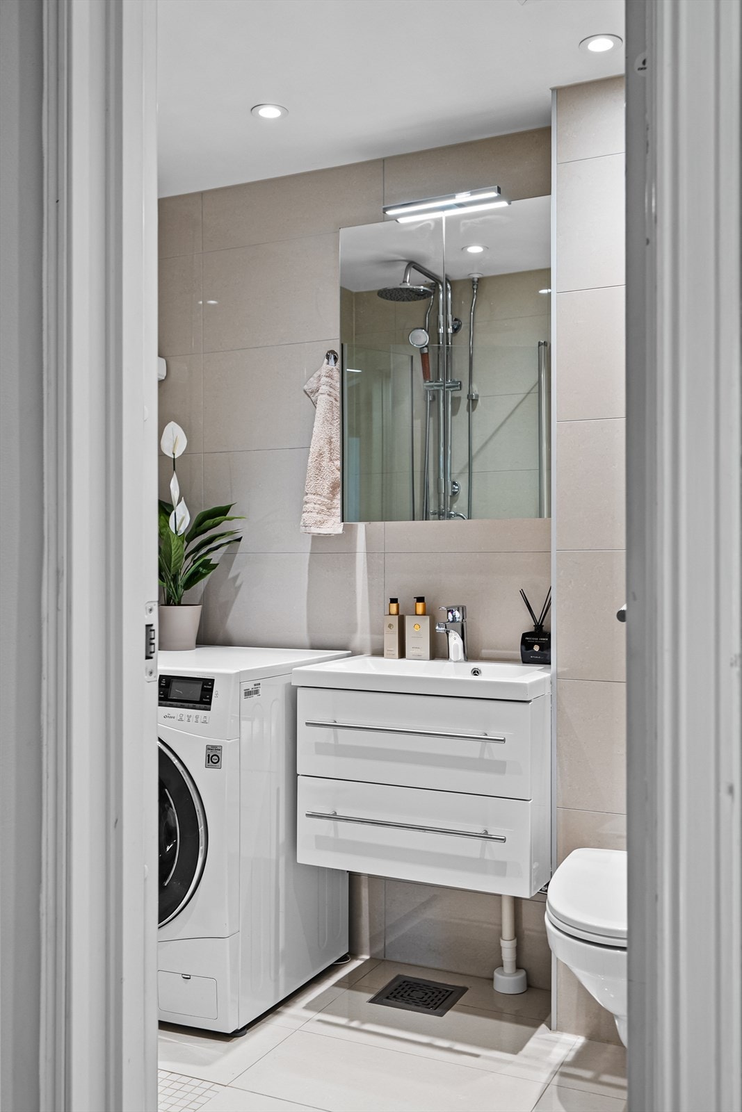 Badet har flislagt gulv med elektriske varmekabler og flislagte vegger, med ett moderne uttrykk. Det er varmekabler i gulvet, og praktisk opplegg for vaskemaskin. Galleribilde