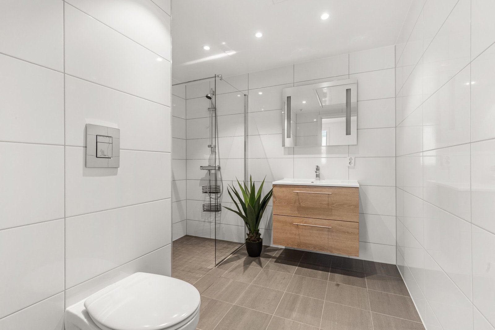 Delikat baderom utført som prefabrikkert baderomskabin med flislagte vegger og gulv, vannbåren gulvvarme samt himling med innfelte LED-downlights. Galleribilde