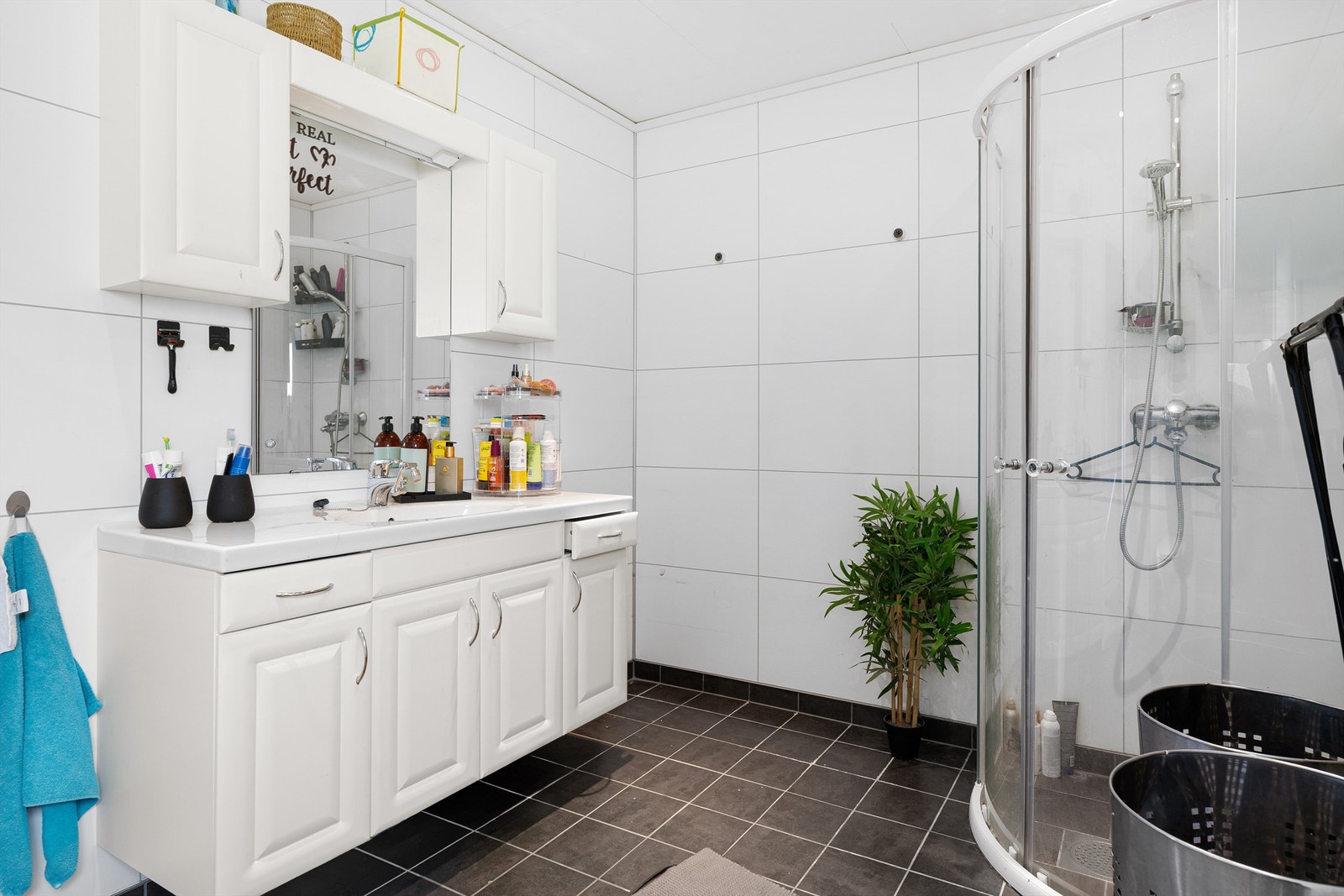 Badet i hovedetasjen har flis på gulvet, baderomsplater på veggene, innredning med nedfelt servant og dusj på vegg med dører. Galleribilde