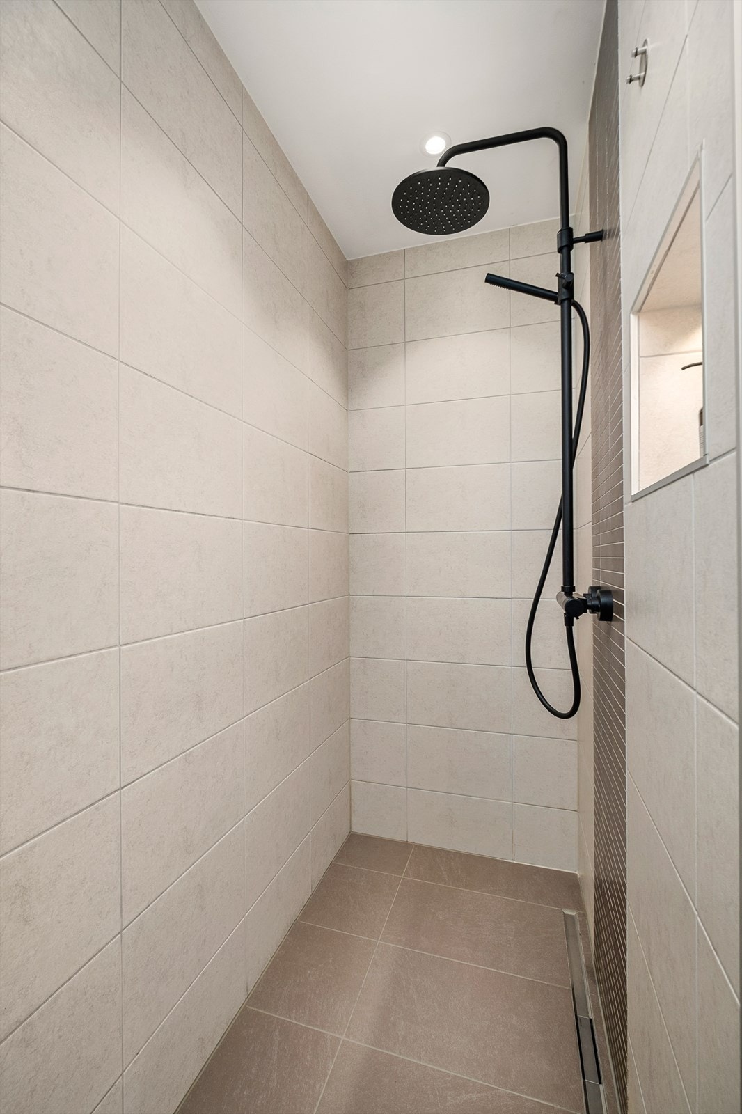 Badet har en romslig dusjsone med både takdusj og hånddusj. Badet er videre innredet med badekar, vegghengt toalett og praktiske oppbevaringsløsninger i en gjennomført utførelse. Galleribilde