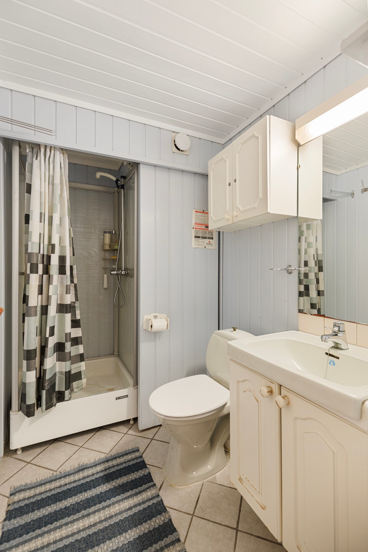 Badet i etasjen har flis på gulv og panel på vegger. Rommet er utstyrt med dusjkabinett, toalett og baderomsinnredning med servant Galleribilde