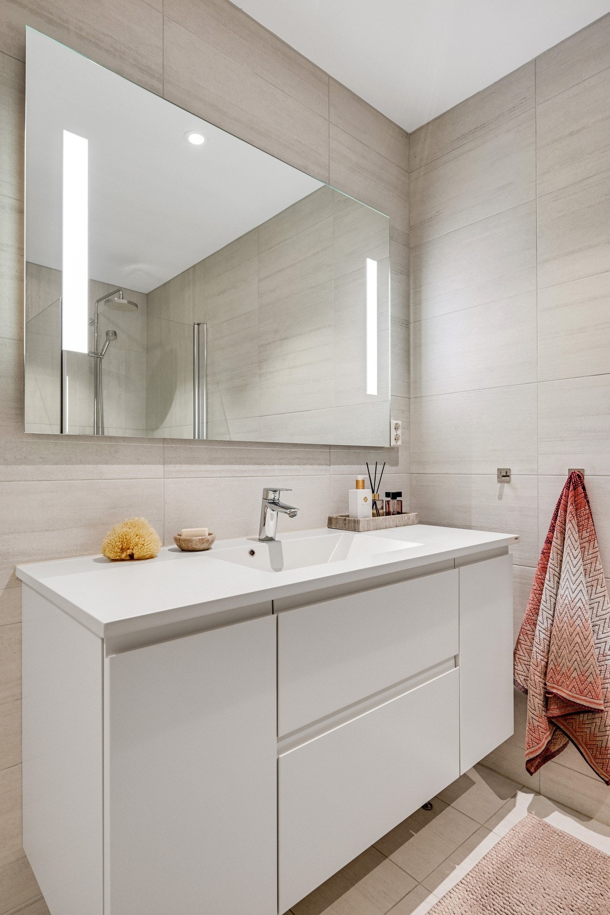 Stort speil på veggen over den pene badromsinnredningen. Det er spot i taket på badet. Galleribilde