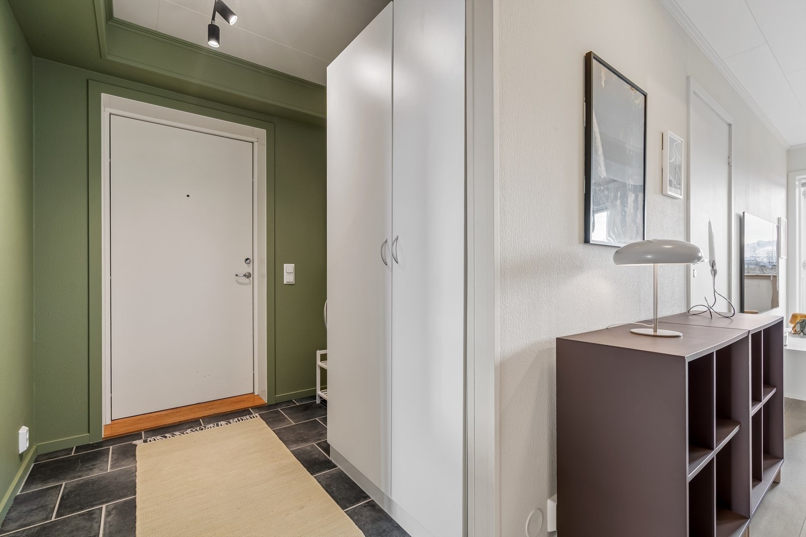 Du ønskes velkommen inn i en innbydende entré med vegger malt i en moderne mørk grønntone - Entreen er utstyrt med et praktisk dobbelt garderobeskap (medfølger). Galleribilde