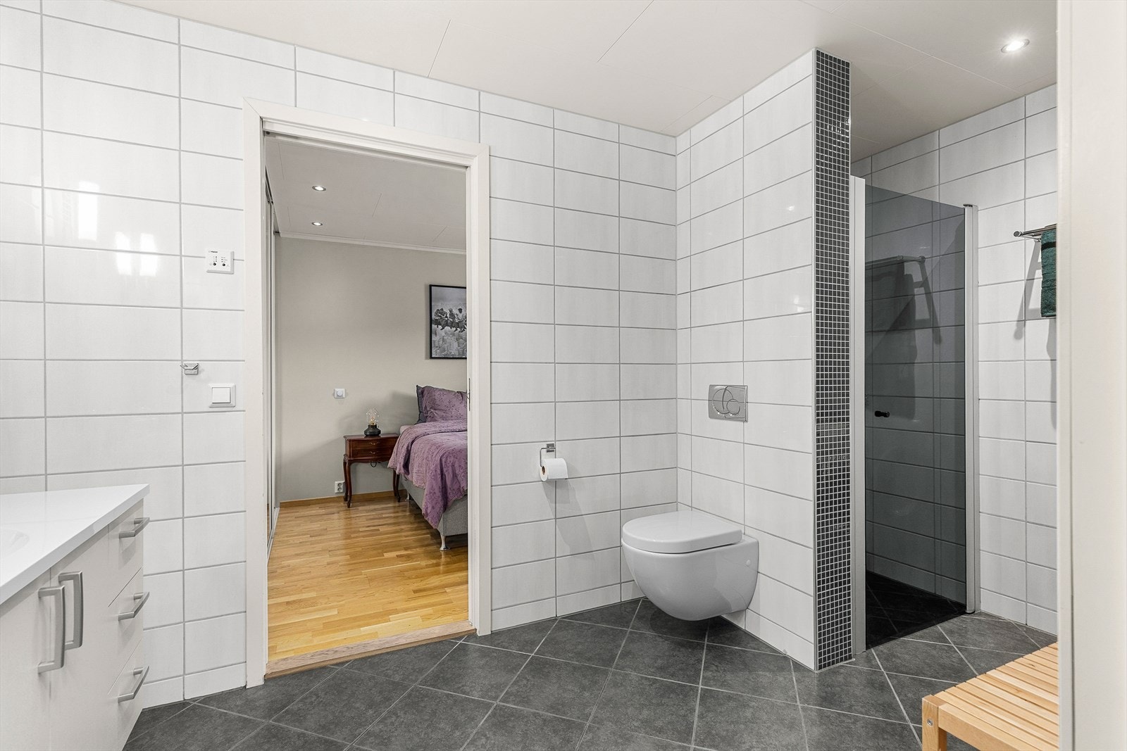Badet er utstyrt med dusjnisje med innfellbare dusjdør. baderomsinnredning, vegghengt klosett og opplegg for vaskemaskin. Galleribilde