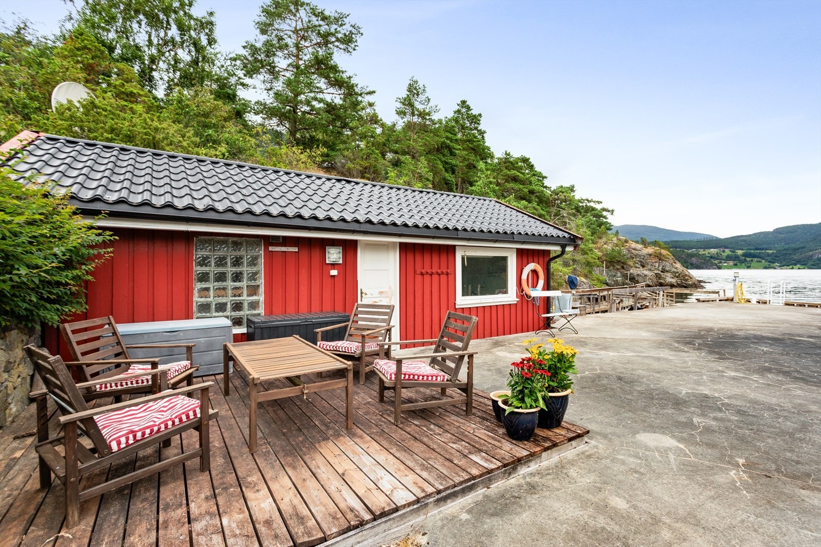 Ved brygga står eit sjarmerande, raudmåla naust, og framfor bygningen er det etablert ein lun sitjeplass på tredekke. Naustet er oppført i ca 1965 Galleribilde