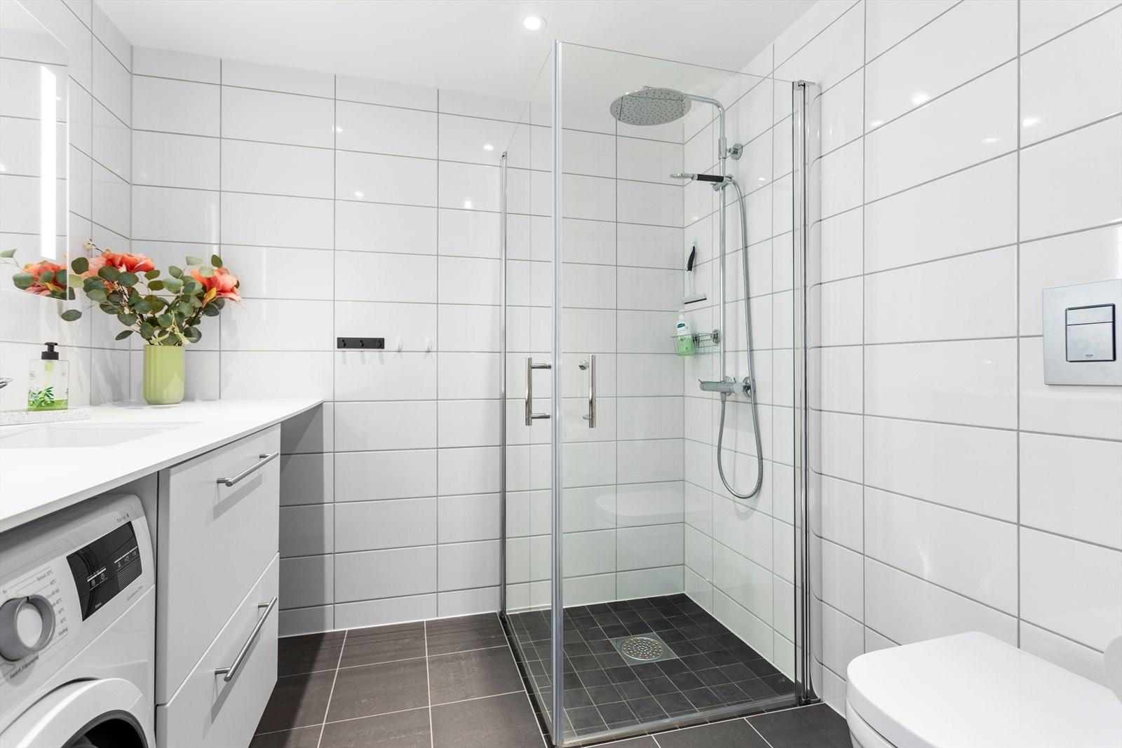Badet er innreidd med vegghengt toalett, dusjhjørne med glasdører, baderomsinnreiing med nedfelt servant og spegel med integrert lys. Galleribilde