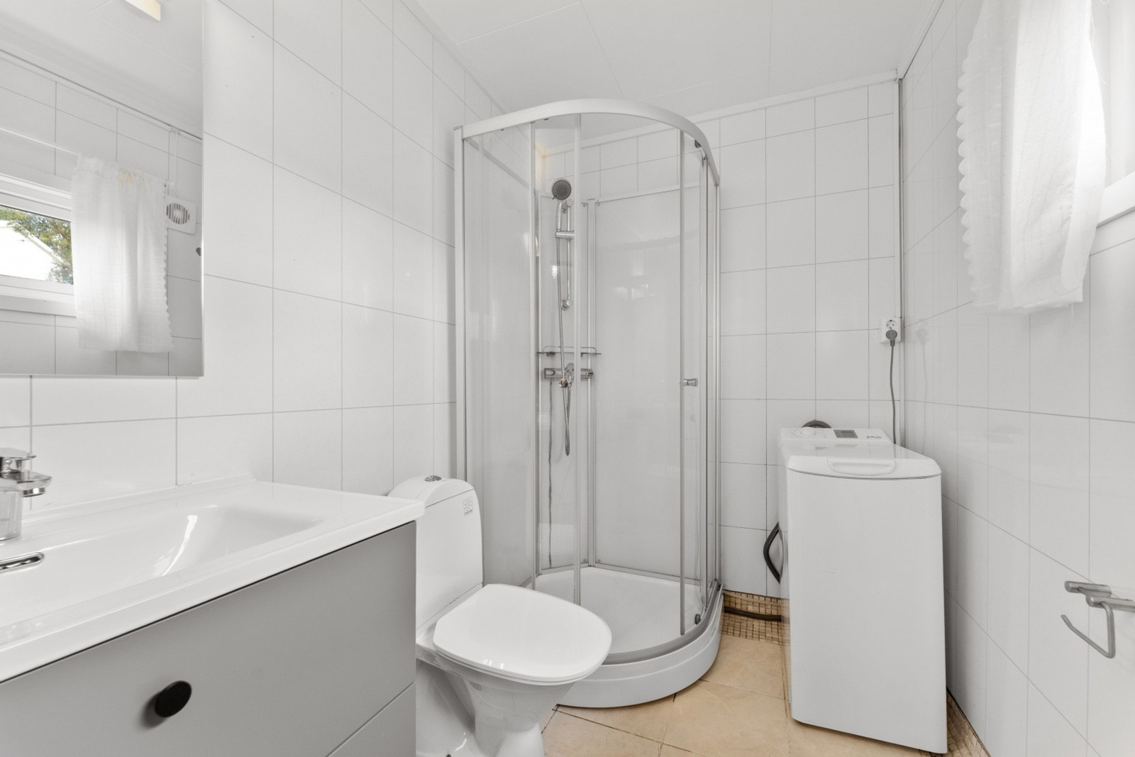 Veggene har baderomsplater, gulv er flislagt og det er opplegg for vaskemaskin. Galleribilde