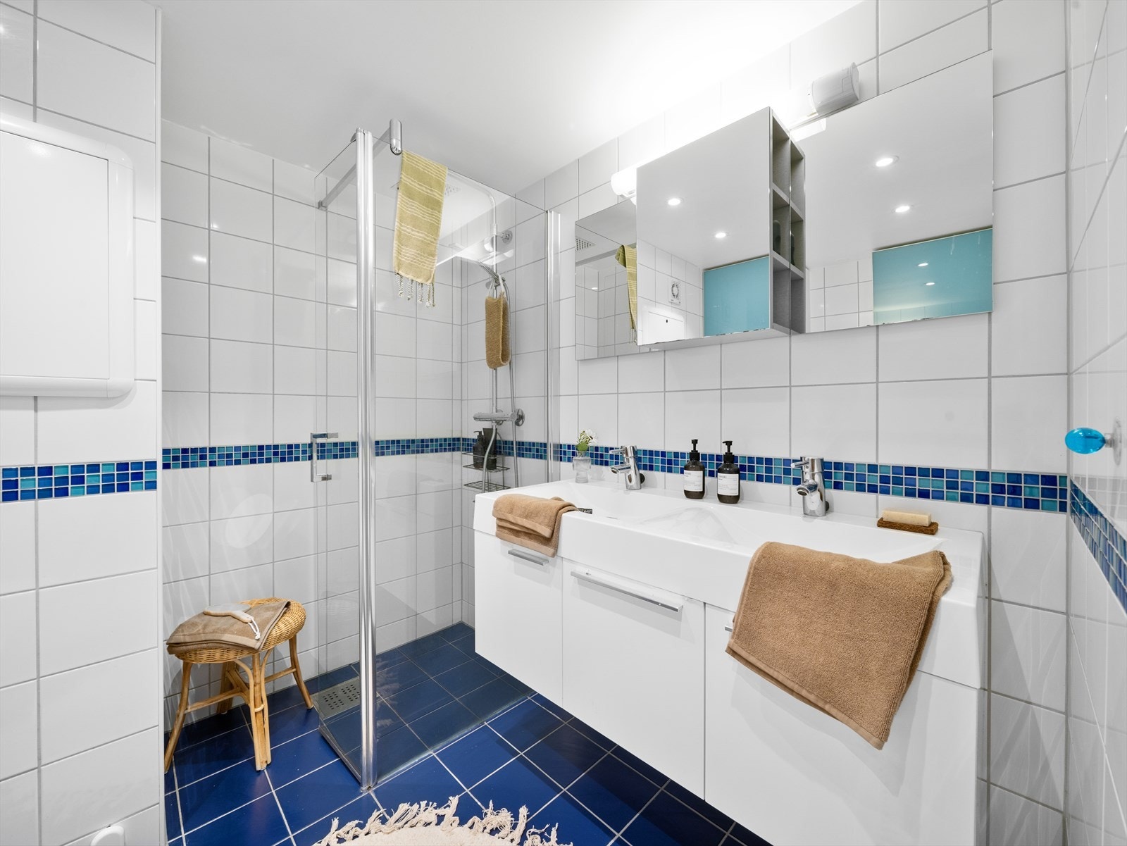 Badet innehar veggmontert toalett, bidé, dusjhjørne og dobbel servant med innredning. Downlights i rak og varme i gulv Galleribilde