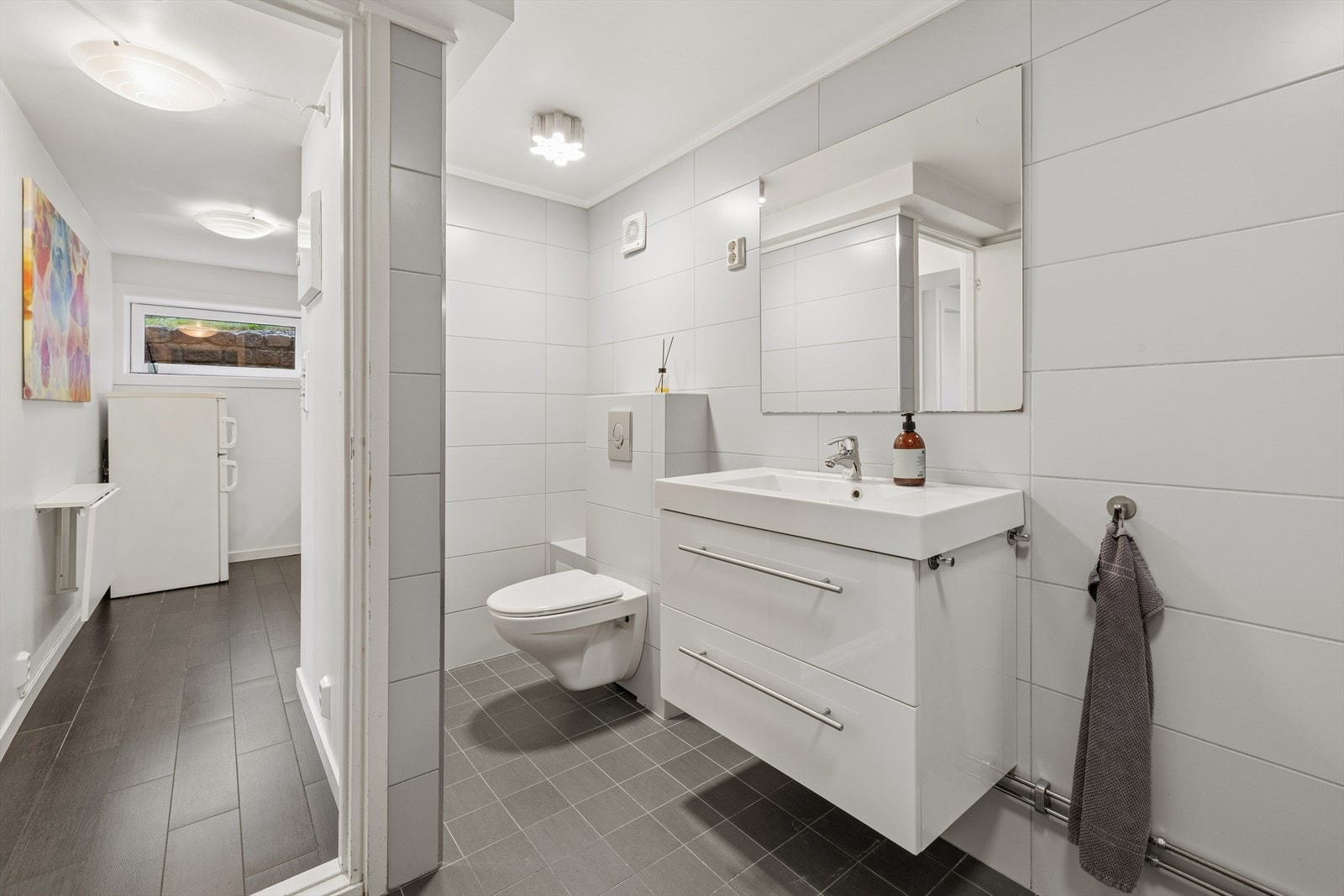 Badet er utstyrt med vegghengt toalett, servantinnredning og dusjhjørne. Galleribilde