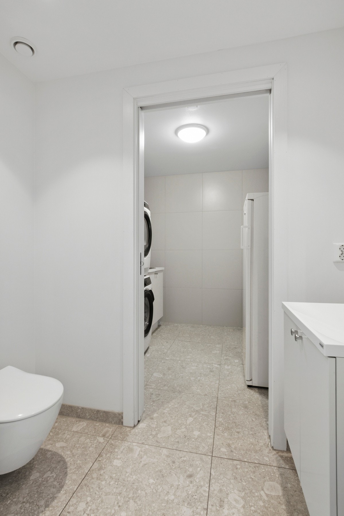 WC-rommet er utstyrt med gulvvarme, vegghengt toalett og et hvitt servantskap med tilhørende speil. Galleribilde