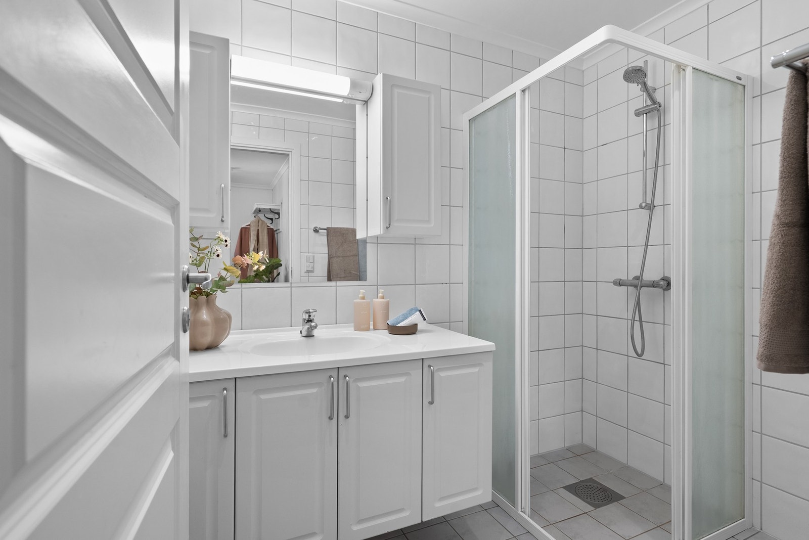 Badet har et praktisk dusjhjørne og gode oppbevaringsmuligheter i servantinnredning med skap, samt skap på hver sin side av speilet Galleribilde