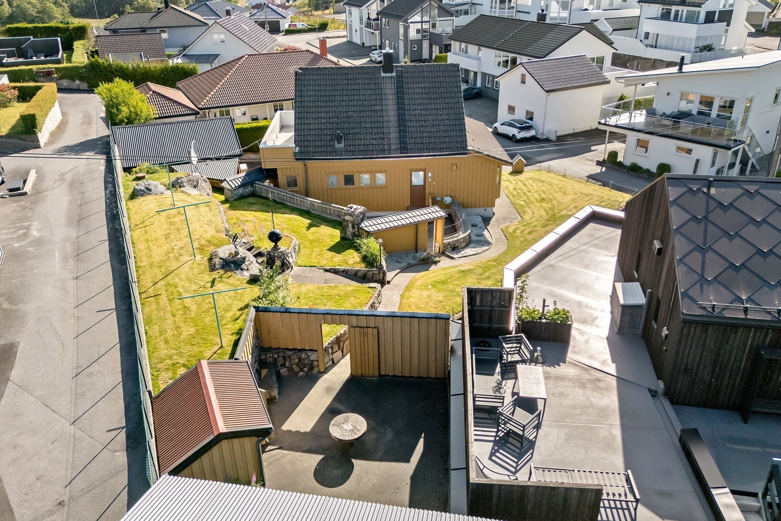 Oversikt over den lettstelte tomten med plen, uteplass og garasje. Galleribilde