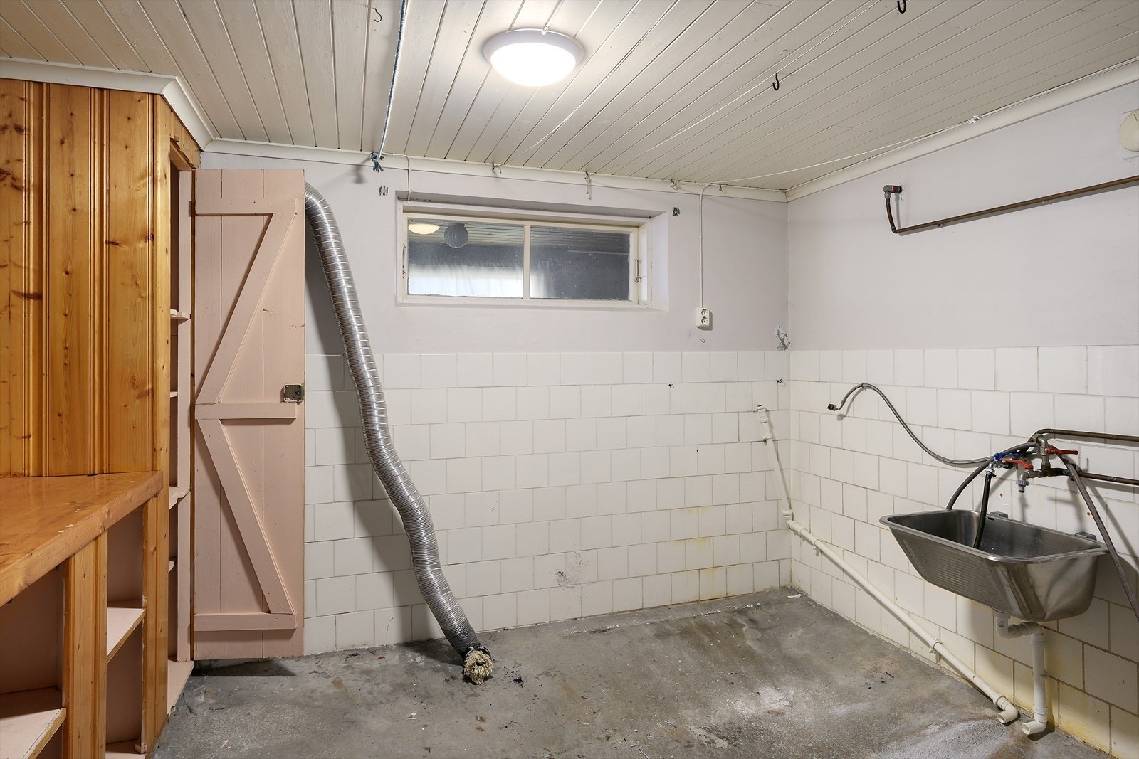 Romslig vaskerom i kjeller med betonggulv, utslagsvask og opplegg for vaskemaskin. Galleribilde