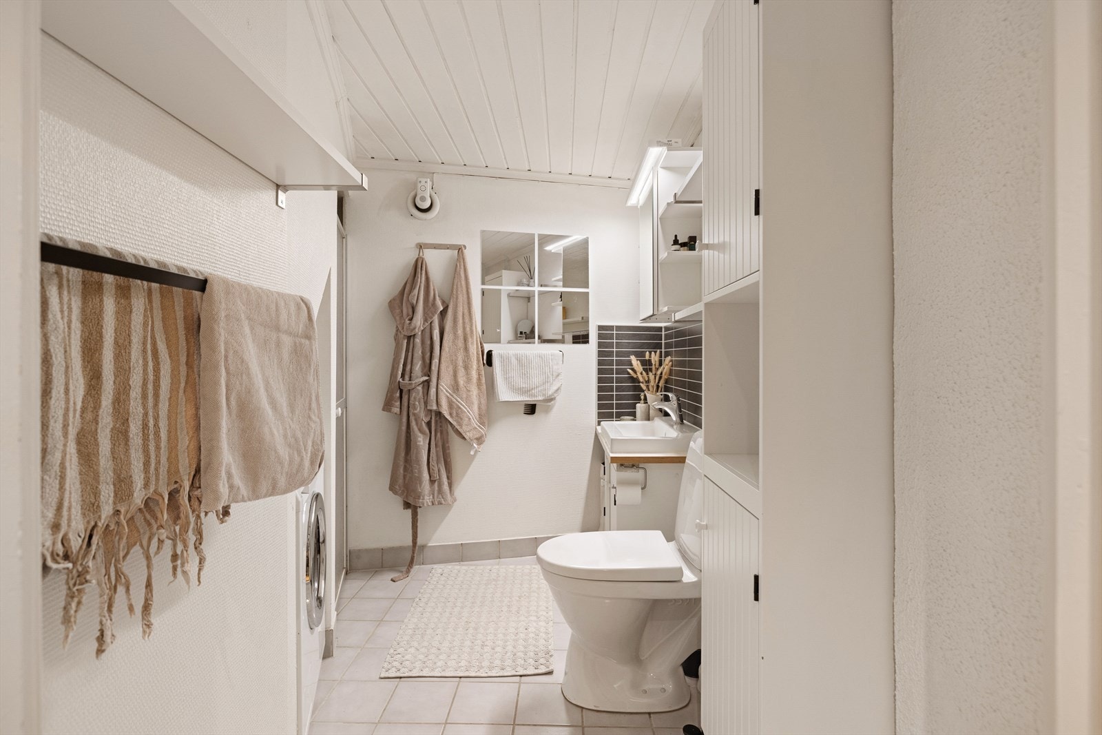 Lyst bad med toalett, dusjnisje, servantinnredning og opplegg for vaskemaskin. Galleribilde