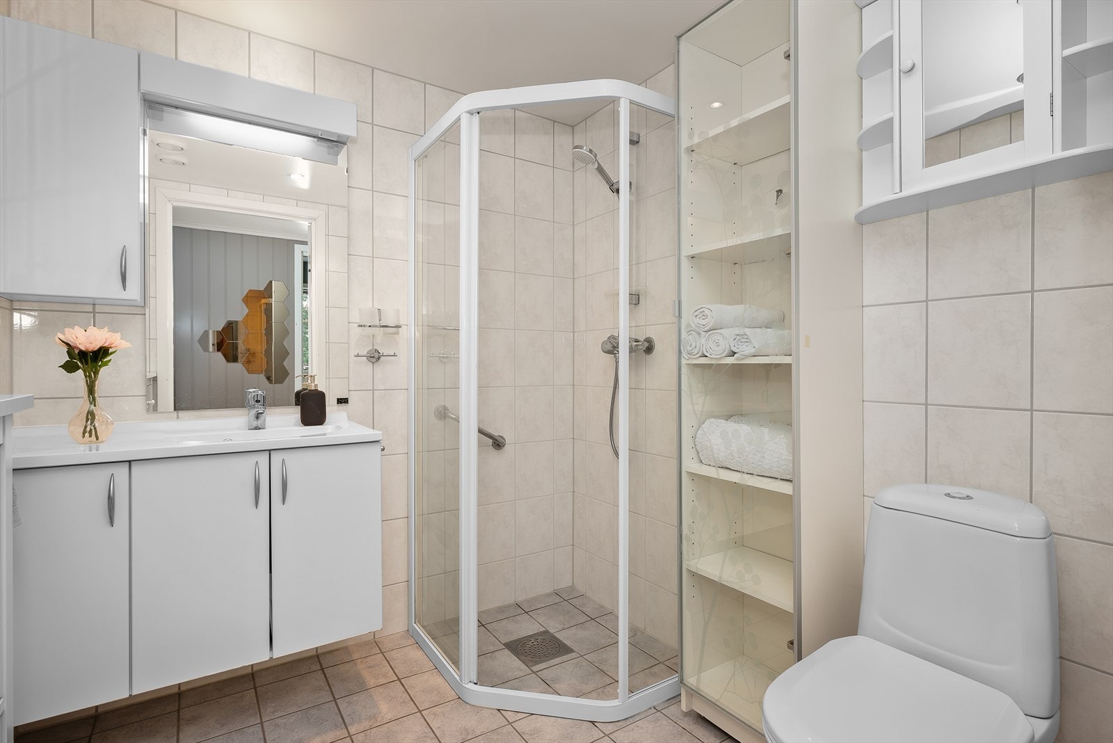 Det flisbelagte badet har et lyst uttrykk og er utstyrt med gulvvarme, dusjhjørne, servantskap, wc og mekanisk avtrekk. Galleribilde
