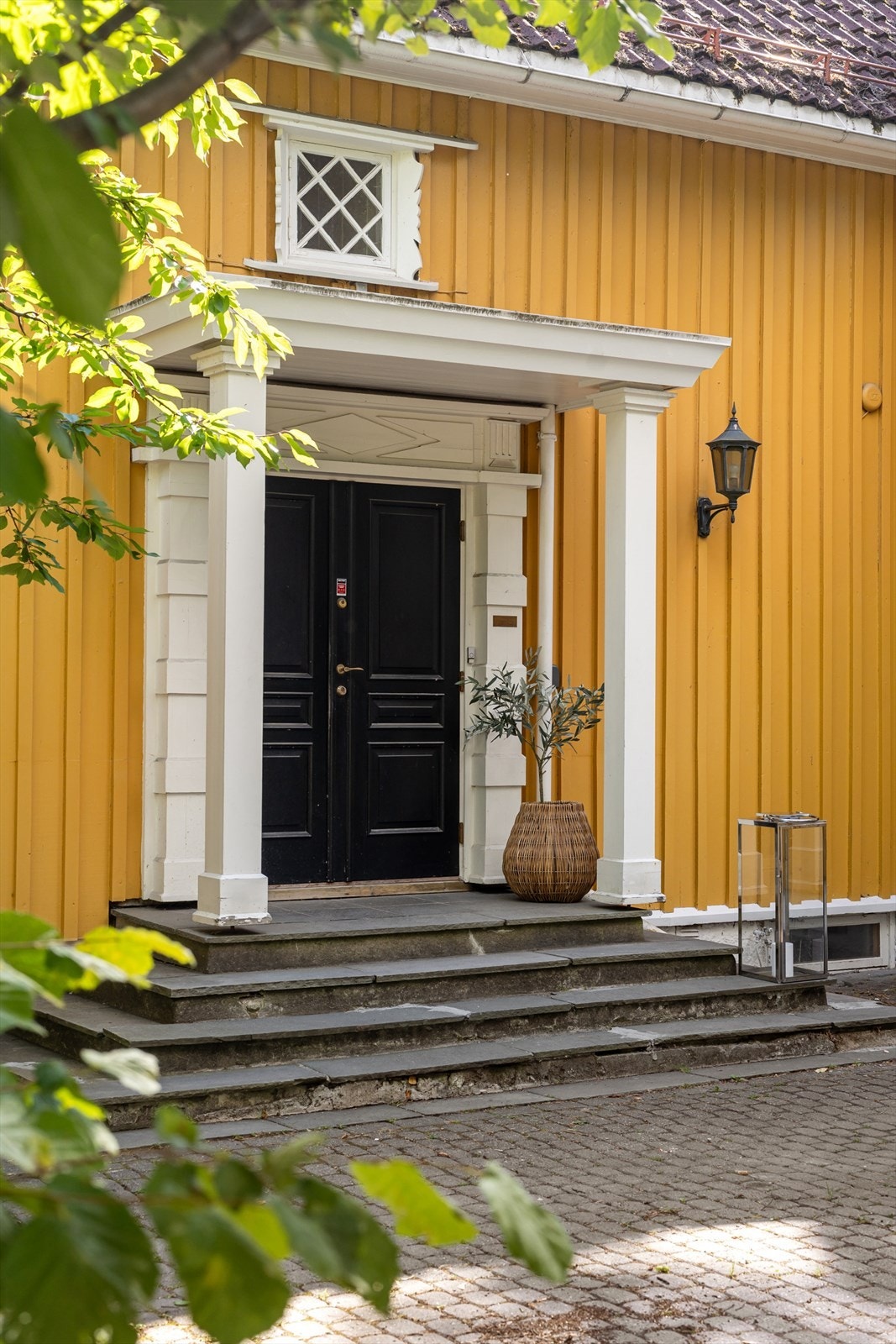 Tofløyet, malt hovedytterdør innrammet av et klassisk inngangsparti med søyler, som fremhever boligens tidstypiske arkitektur og særpreg. Galleribilde