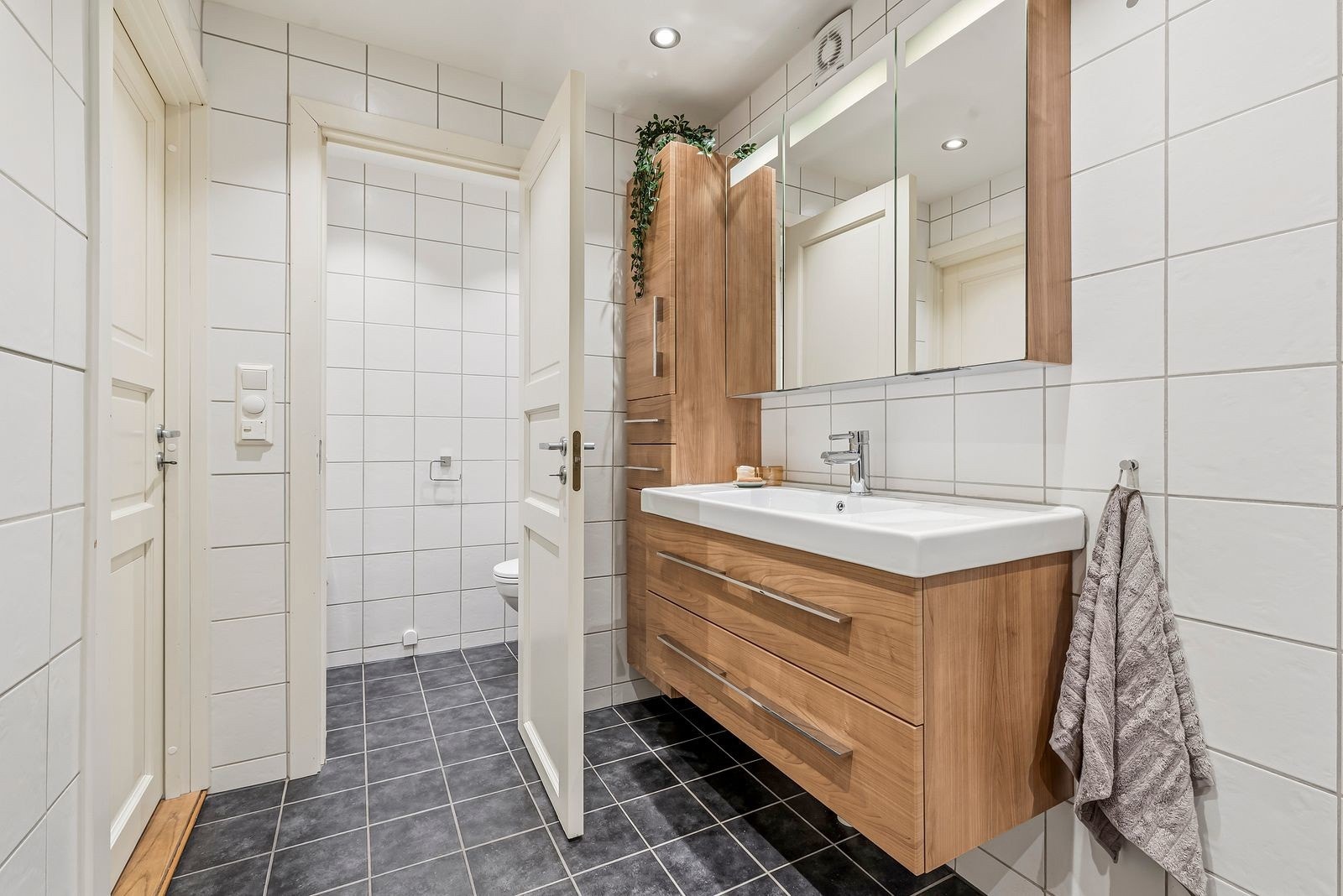 Badet har downlights i taket og er praktisk innredet med servant med skuffer, høyskap, speilskap og dusjhjørne med innadslående glassdører. Det er også opplegg for vaskemaskin. Galleribilde