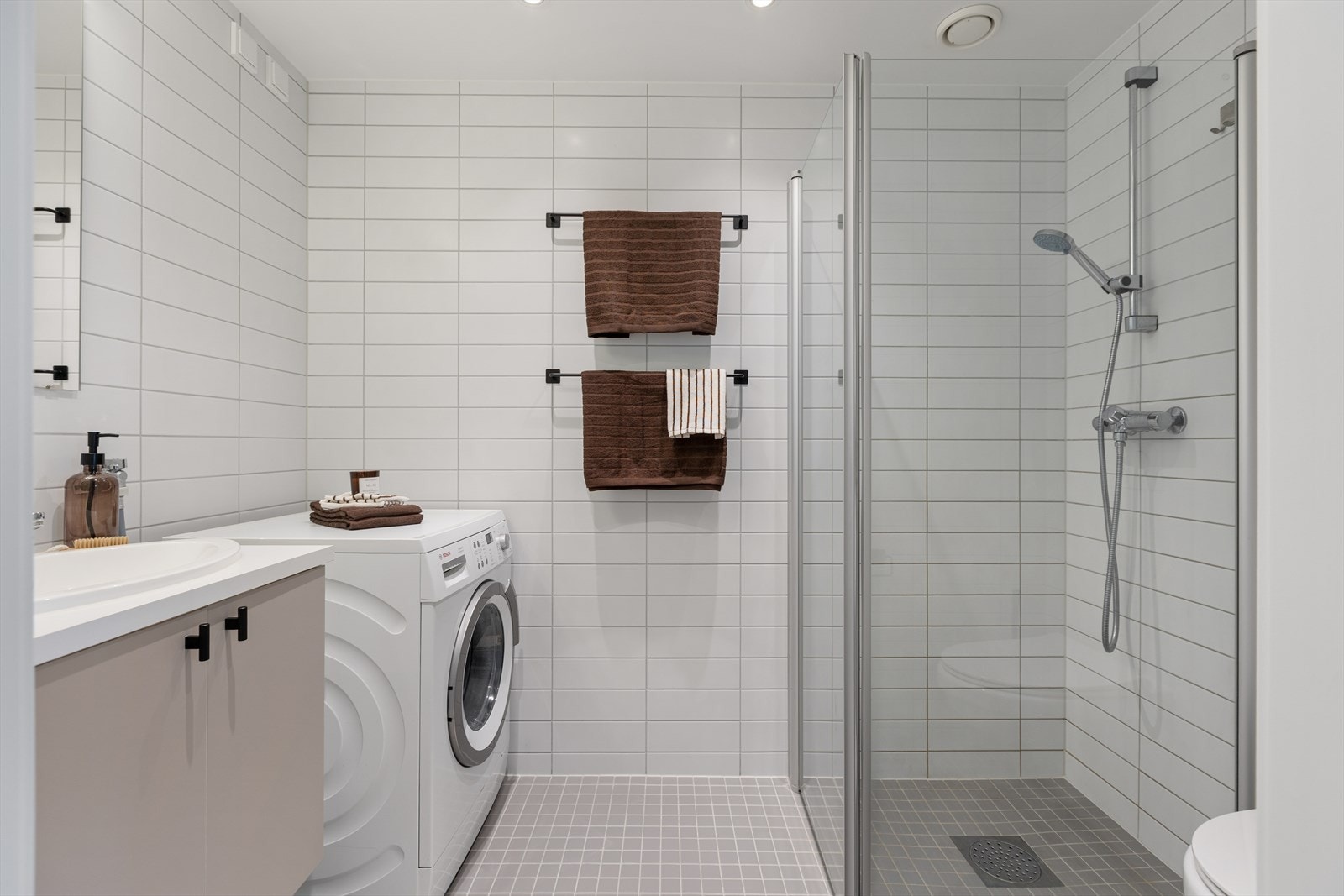 Romslig bad med flislagte overflater, dusjsone og opplegg for vaskemaskin. Galleribilde