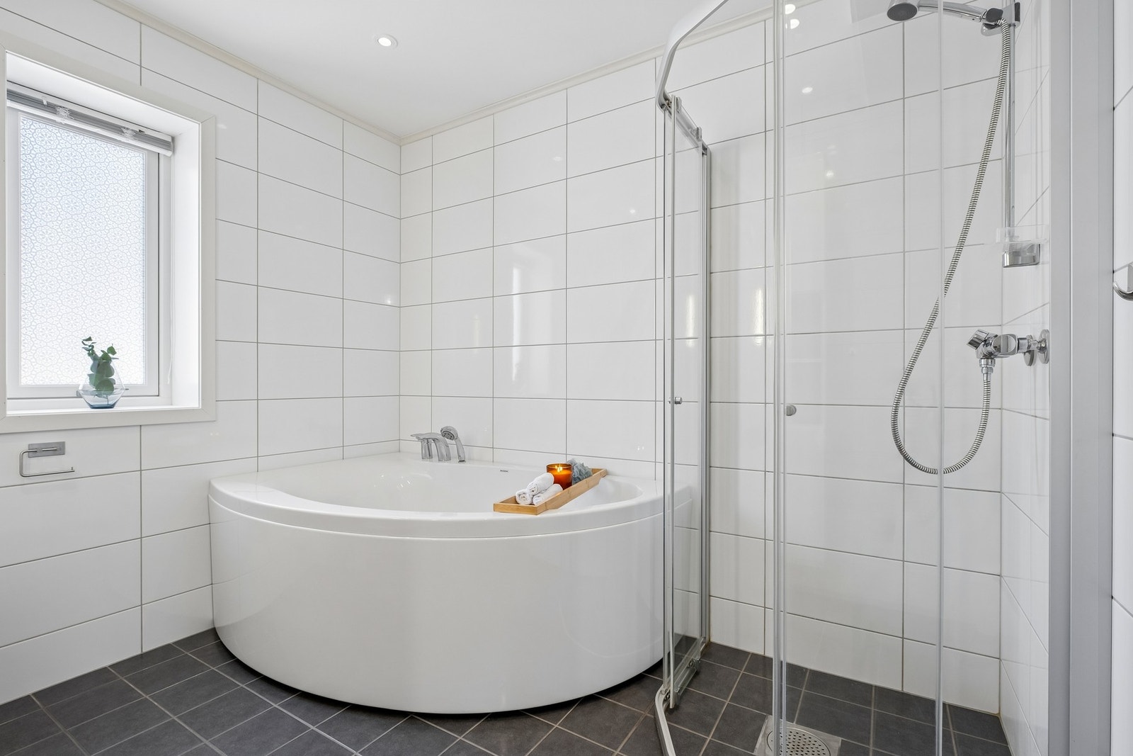 Badet har både dusjkabinett og hjørnebadekar, samt et vindu som gir godt med naturlig lys til rommet. Galleribilde