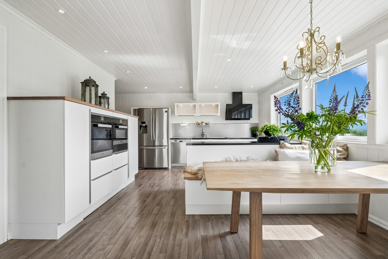 Moderne kjøkken med integrerte hvitevarer, åpen løsning og store vinduer som slipper inn mye naturlig lys. Galleribilde